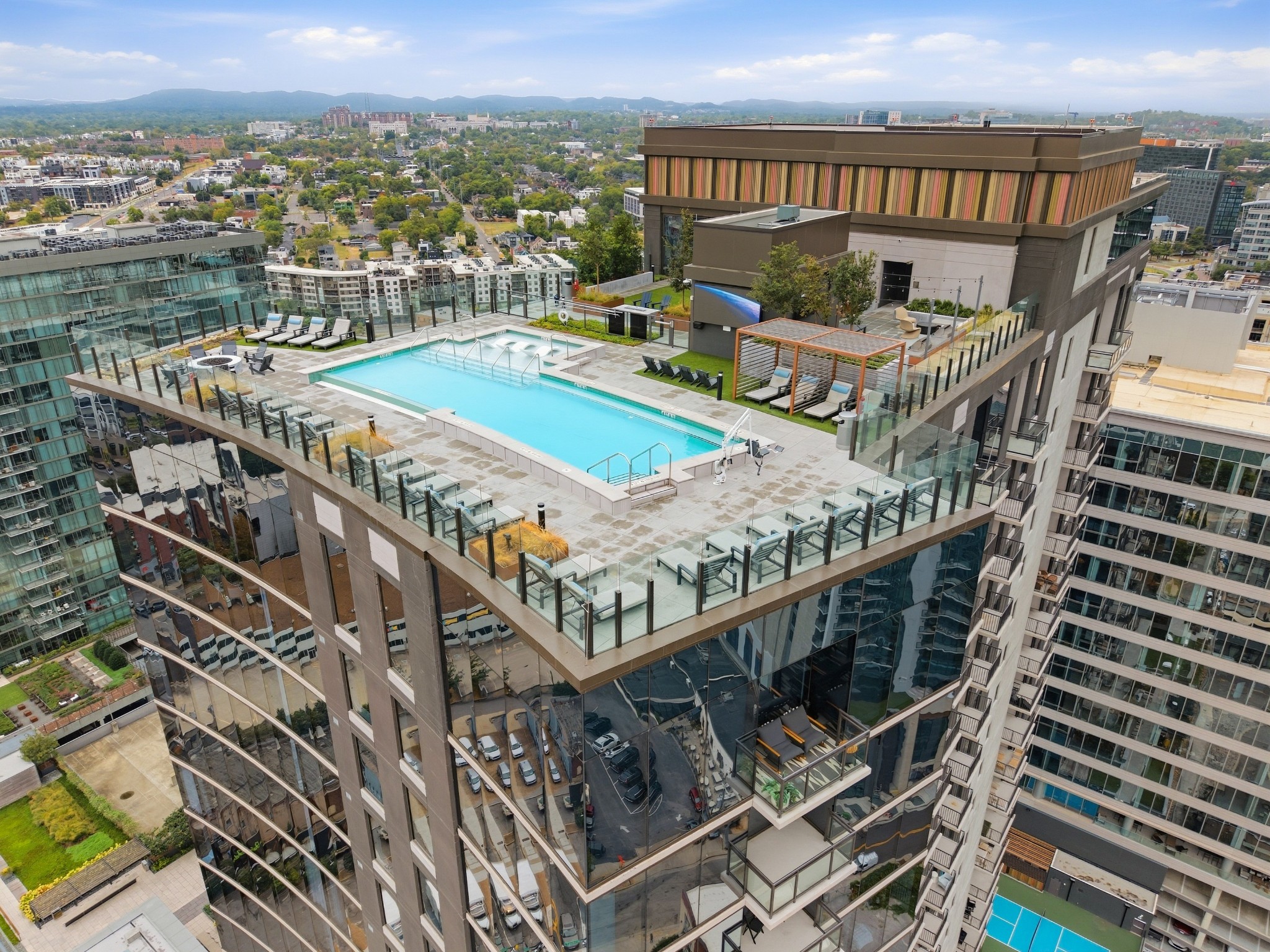 Rooftop pool and lounge deck atop a downtown high-rise, with Nashville buildings and distant hills beyond.
