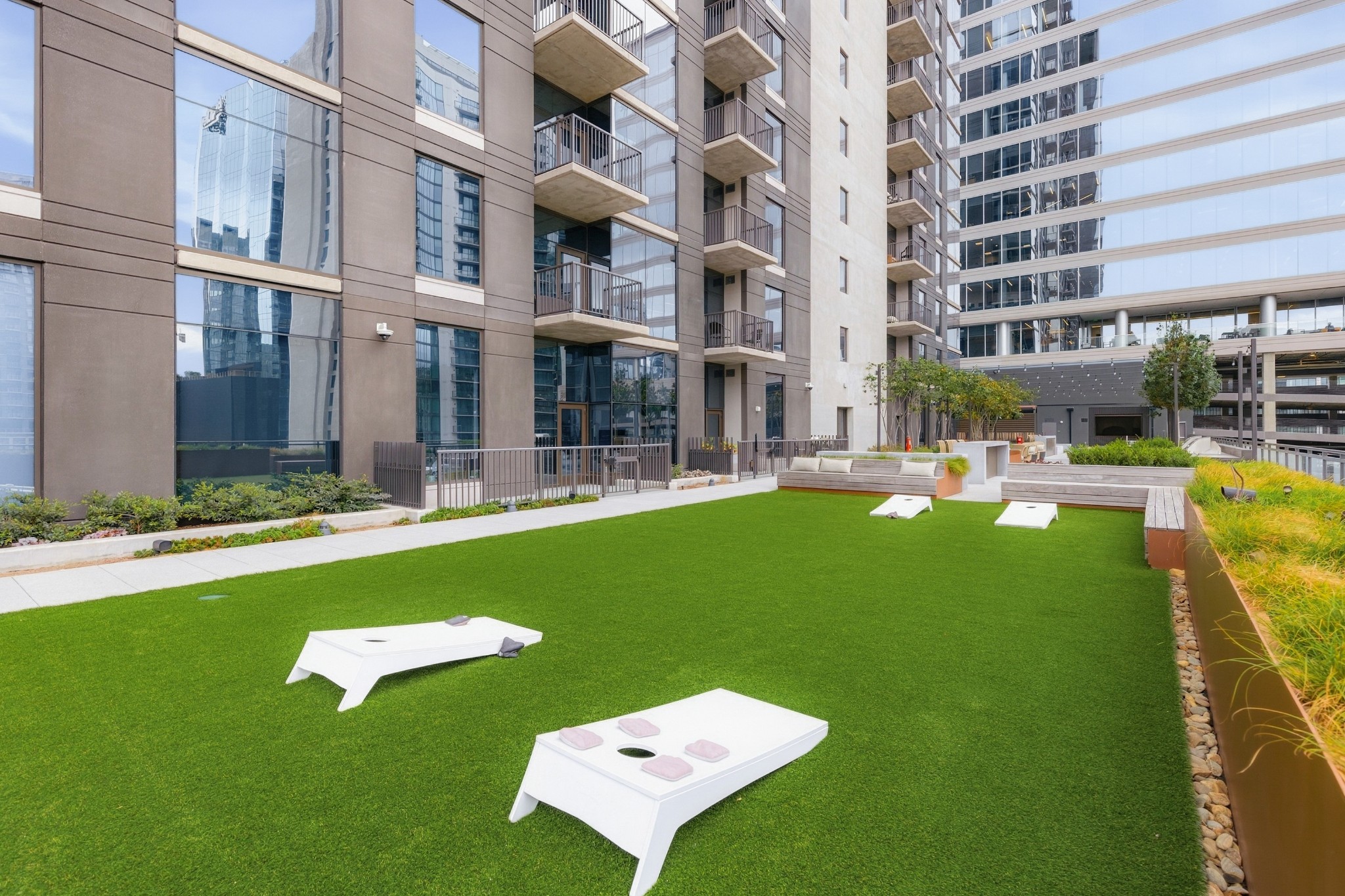 Condominium courtyard with a green lawn, cornhole boards, built-in seating, and balconies.