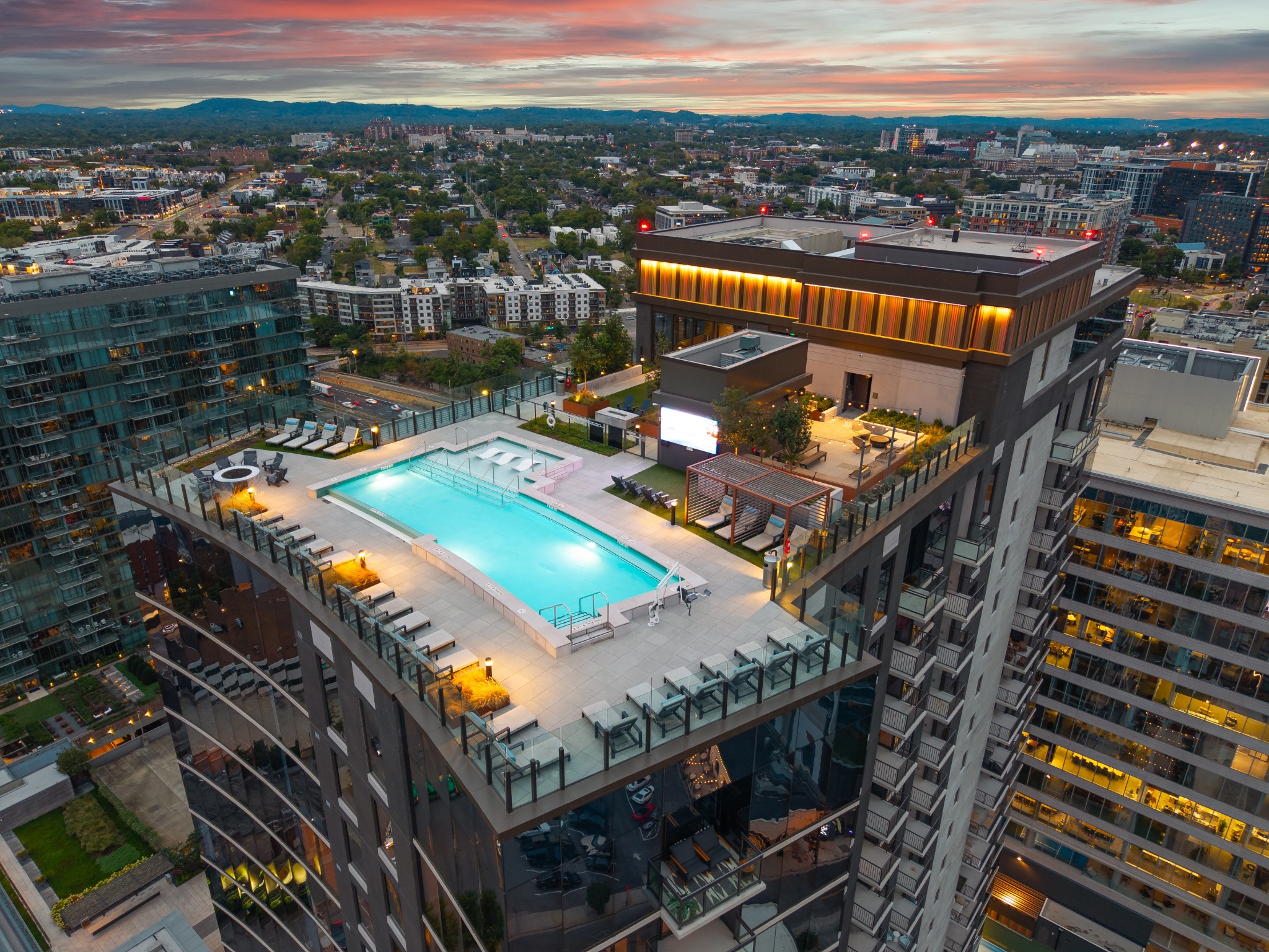 Rooftop pool terrace with lounge chairs and Nashville city skyline at dusk.