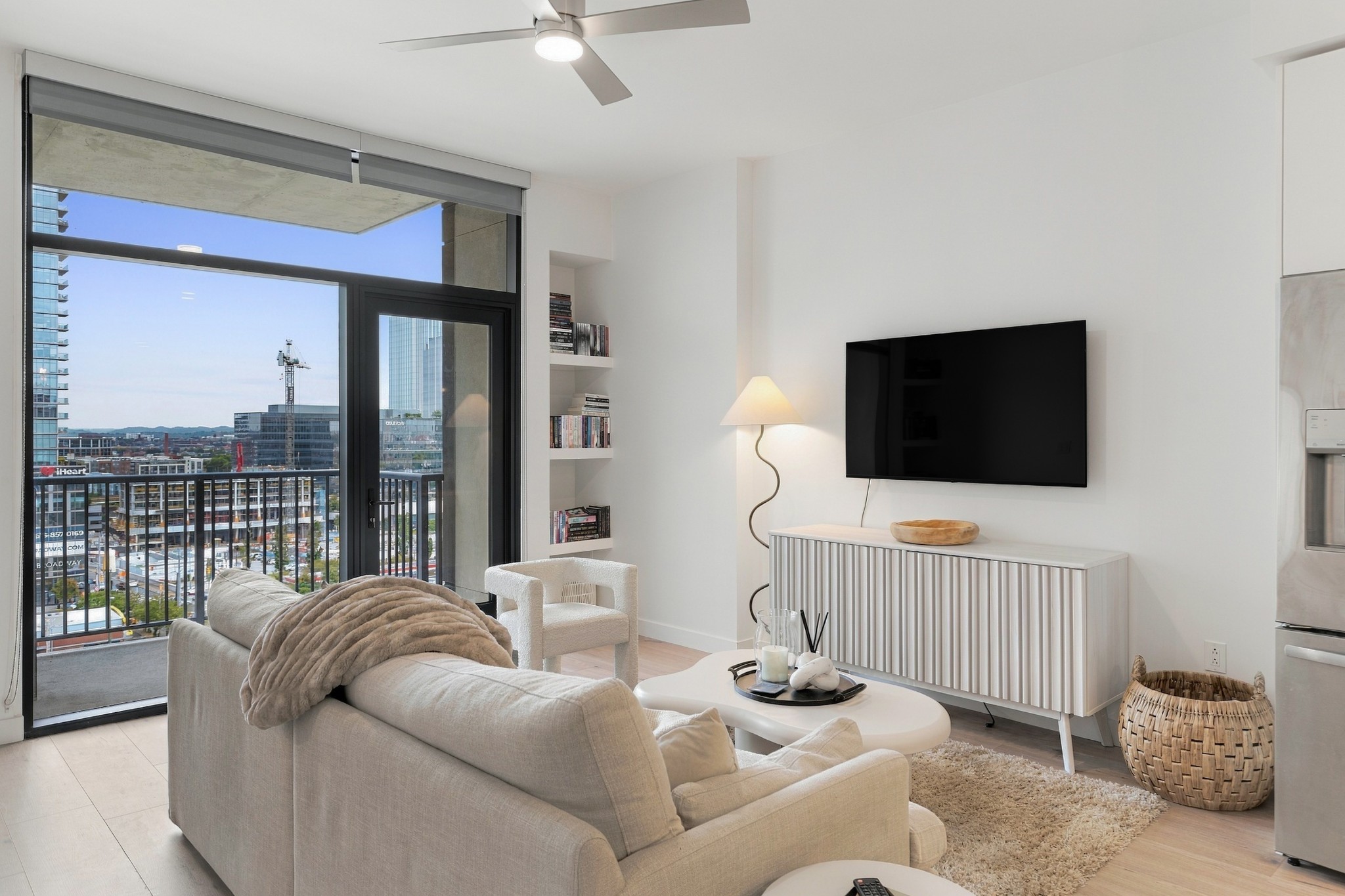 Condo living room with a light sofa and balcony doors overlooking the city skyline.