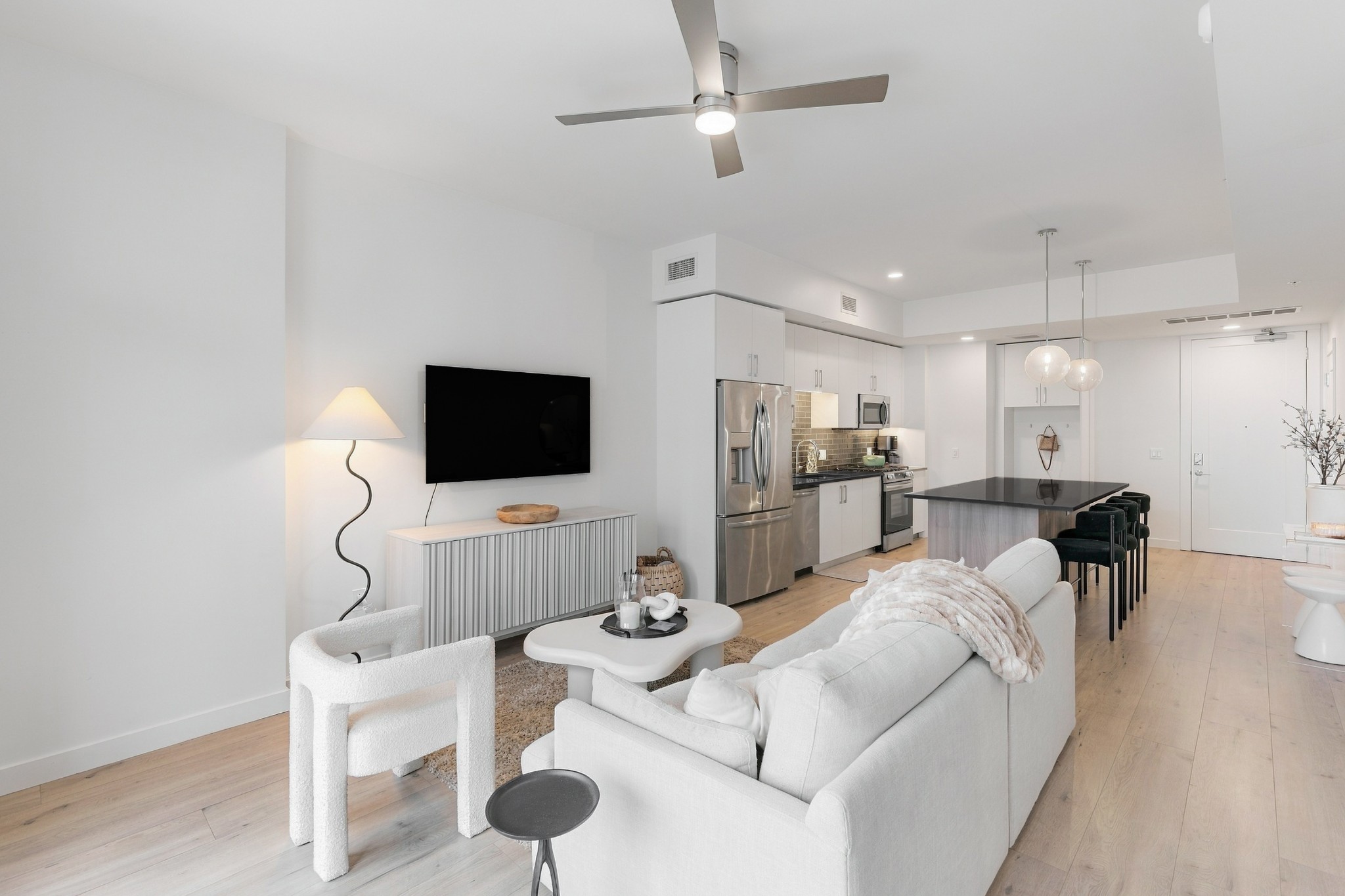 Open-plan condo living room and kitchen with white seating, stainless appliances, and a dark island.