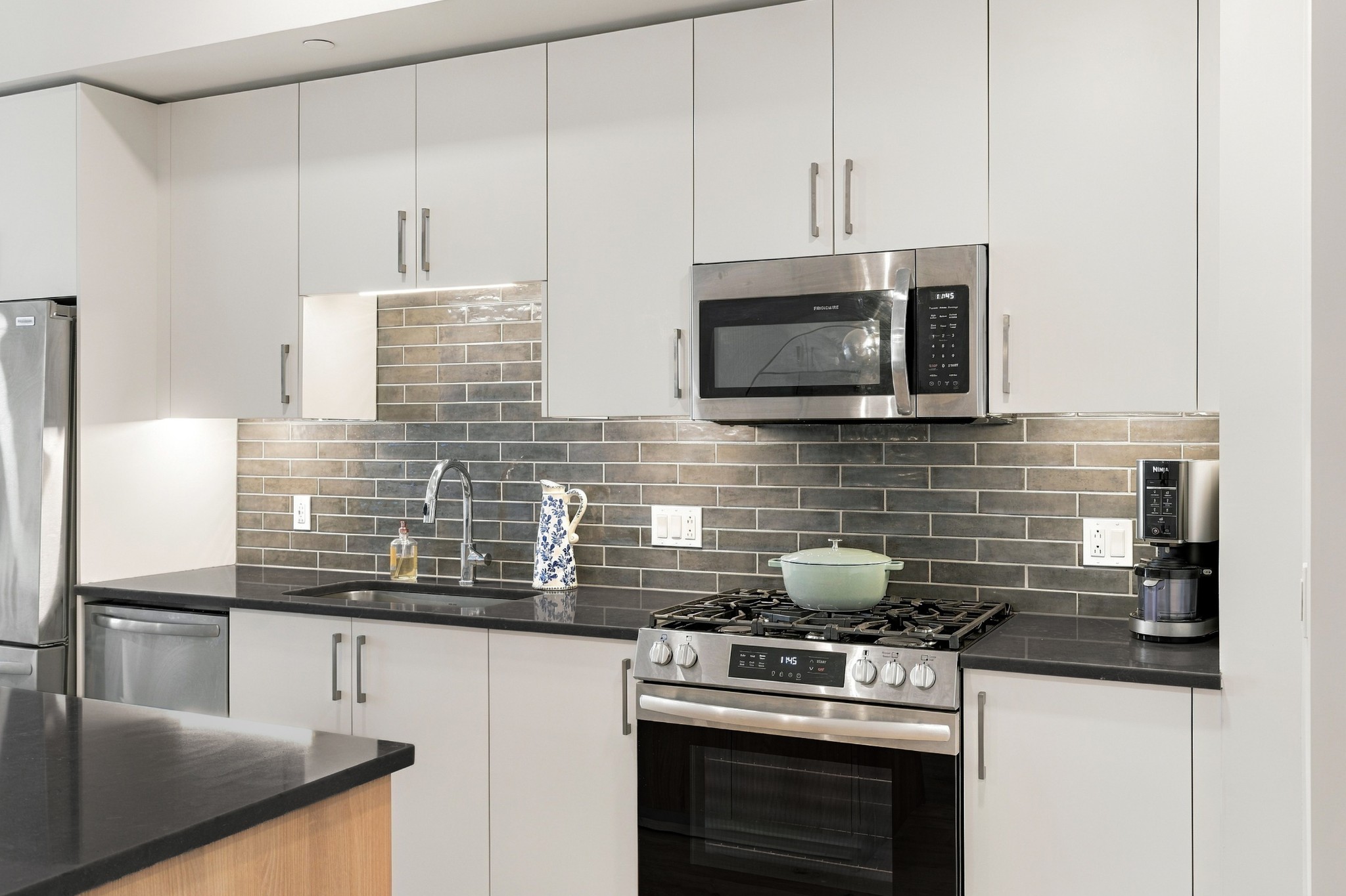 Modern kitchen with white cabinets, gray tile backsplash, stainless steel appliances, and a gas range.