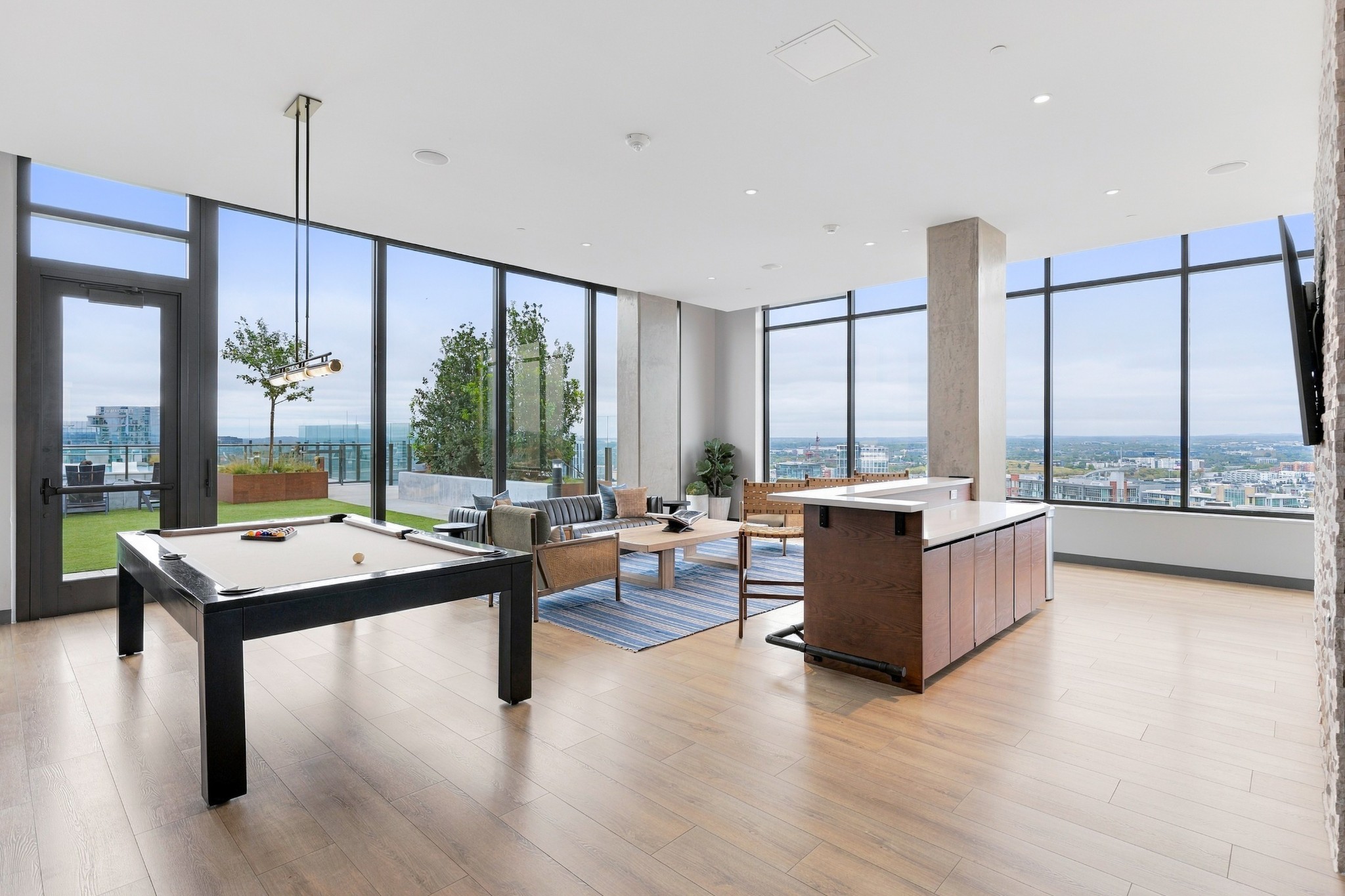Residents’ lounge with a pool table, bar counter, and floor-to-ceiling windows overlooking Nashville.