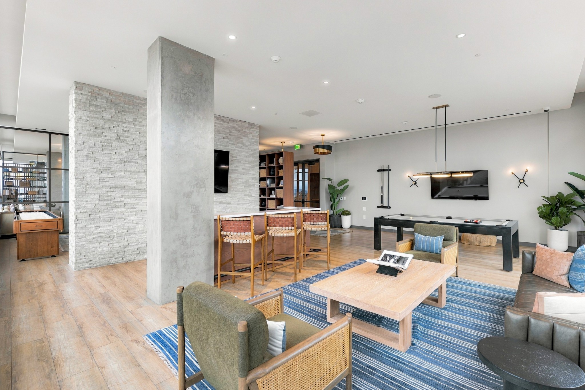 Furnished lounge with a pool table, foosball table, and seating around a blue striped rug.