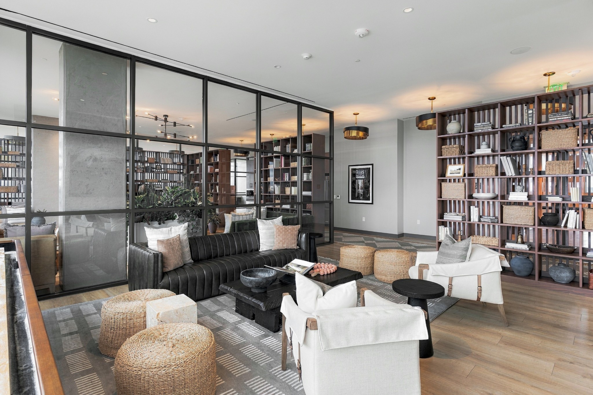 Furnished lounge with floor-to-ceiling bookshelves, a black sofa, white chairs, and woven ottomans.
