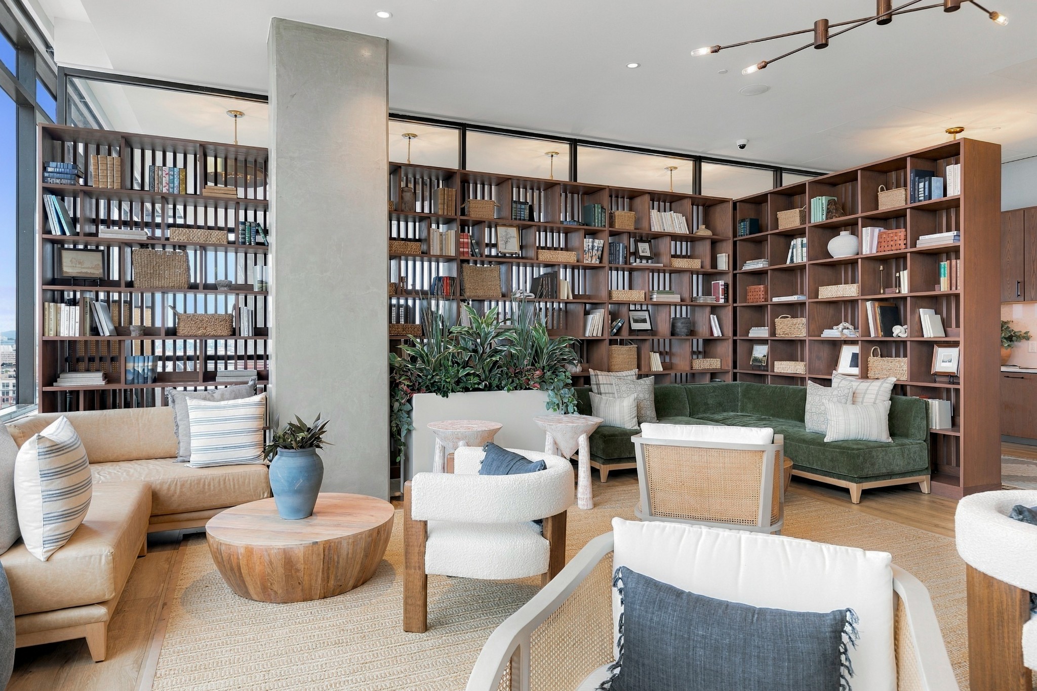 Furnished lounge with floor-to-ceiling bookshelves, green sofa, white chairs, and large windows.