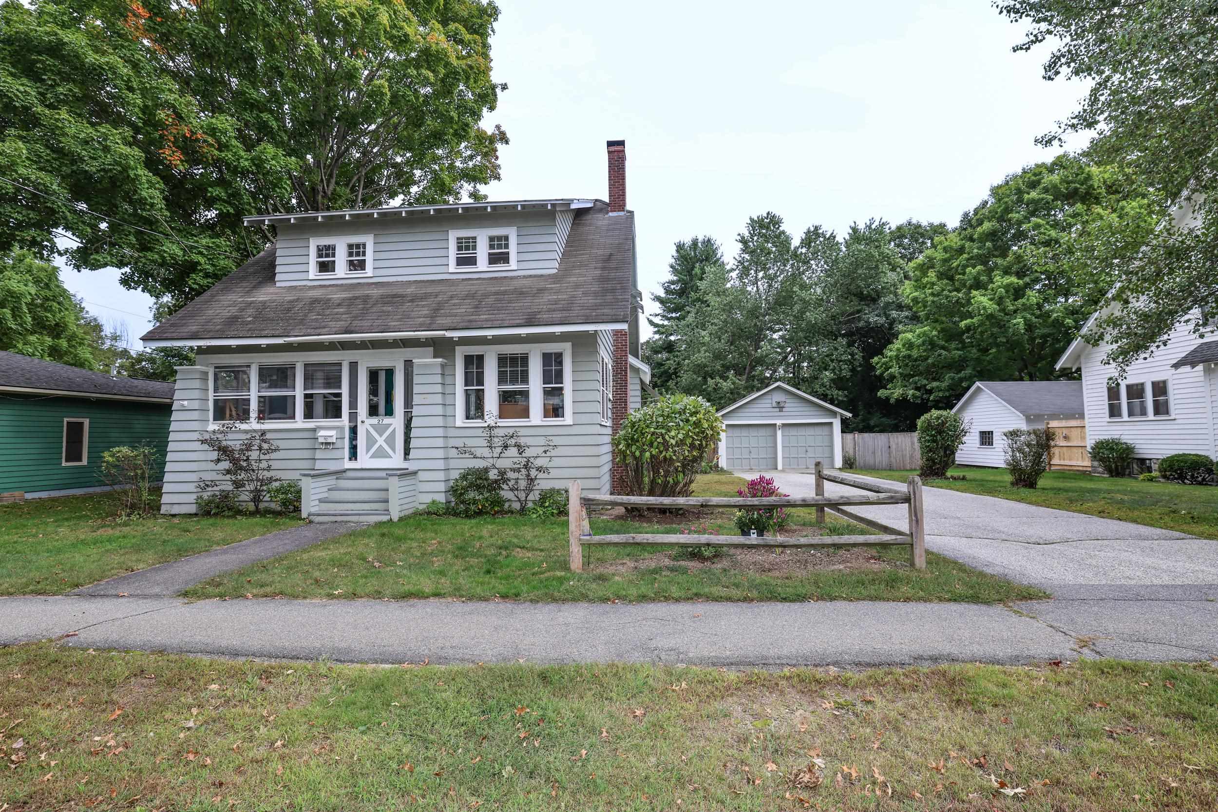Gray house with a broad dormer and brick chimney, beside a driveway leading to a detached garage.