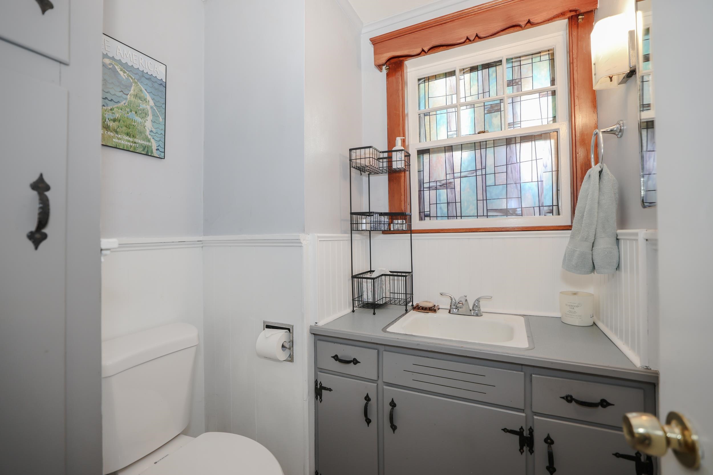 Bathroom with a gray vanity and sink beneath a large stained-glass window framed in wood.