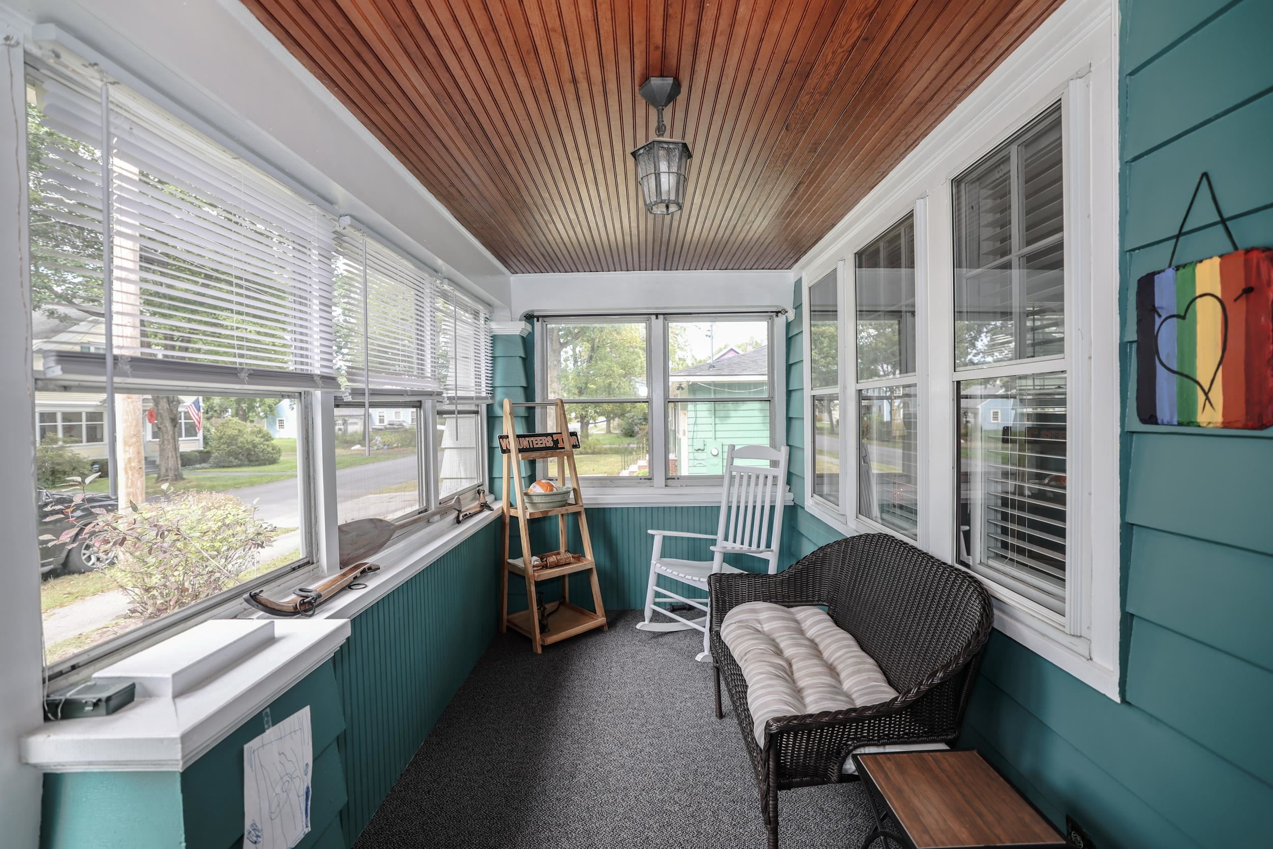 Enclosed teal sunroom with a wood-plank ceiling, broad windows, and a wicker loveseat.