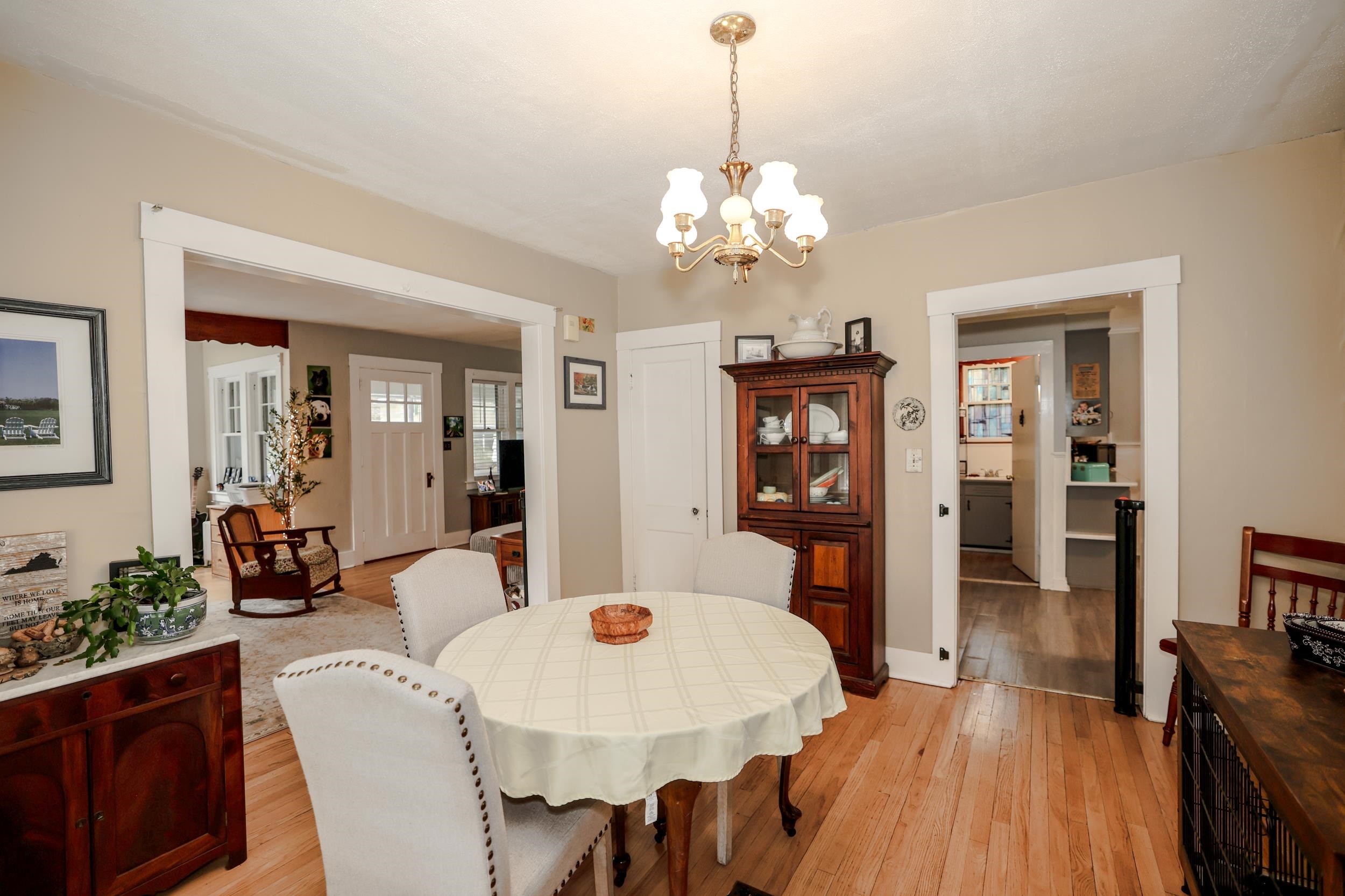Furnished dining room with a round table, brass chandelier, hardwood floors, and a dark wood china cabinet.