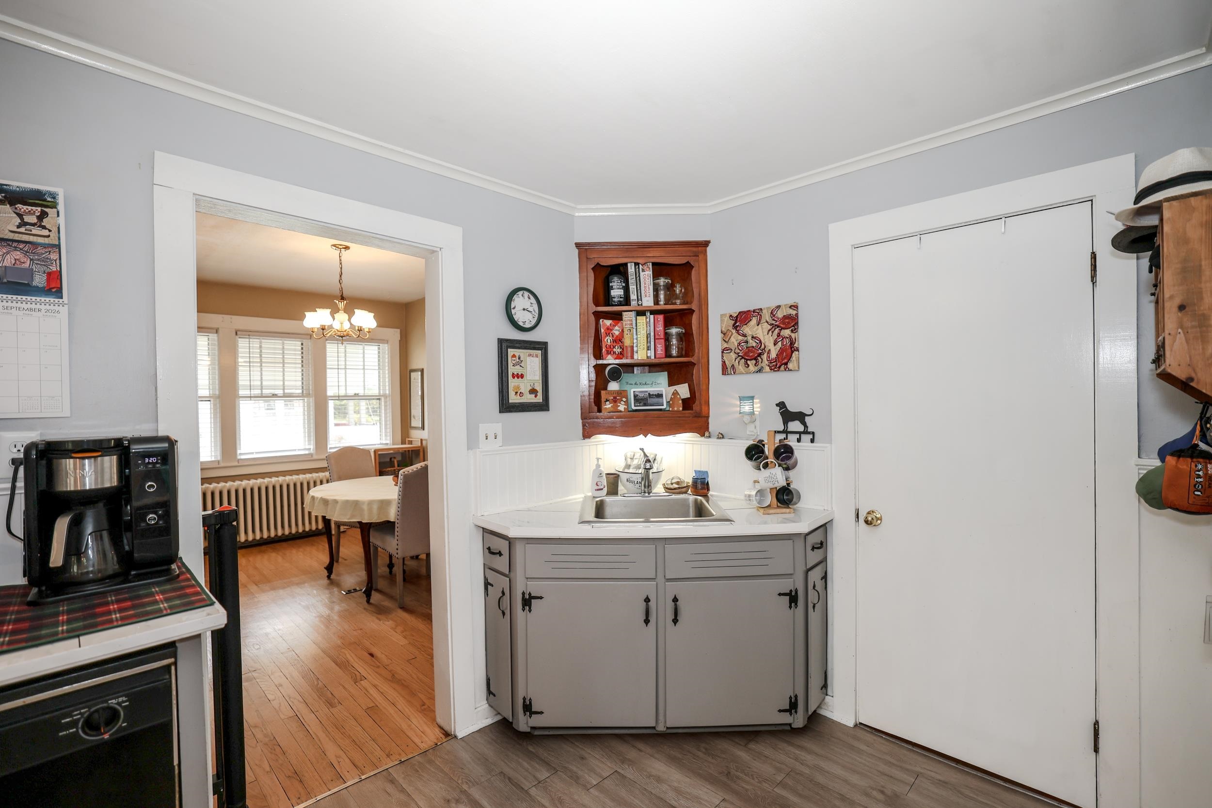 Kitchen with a corner sink and gray cabinets, opening into a bright dining room with wood floors.