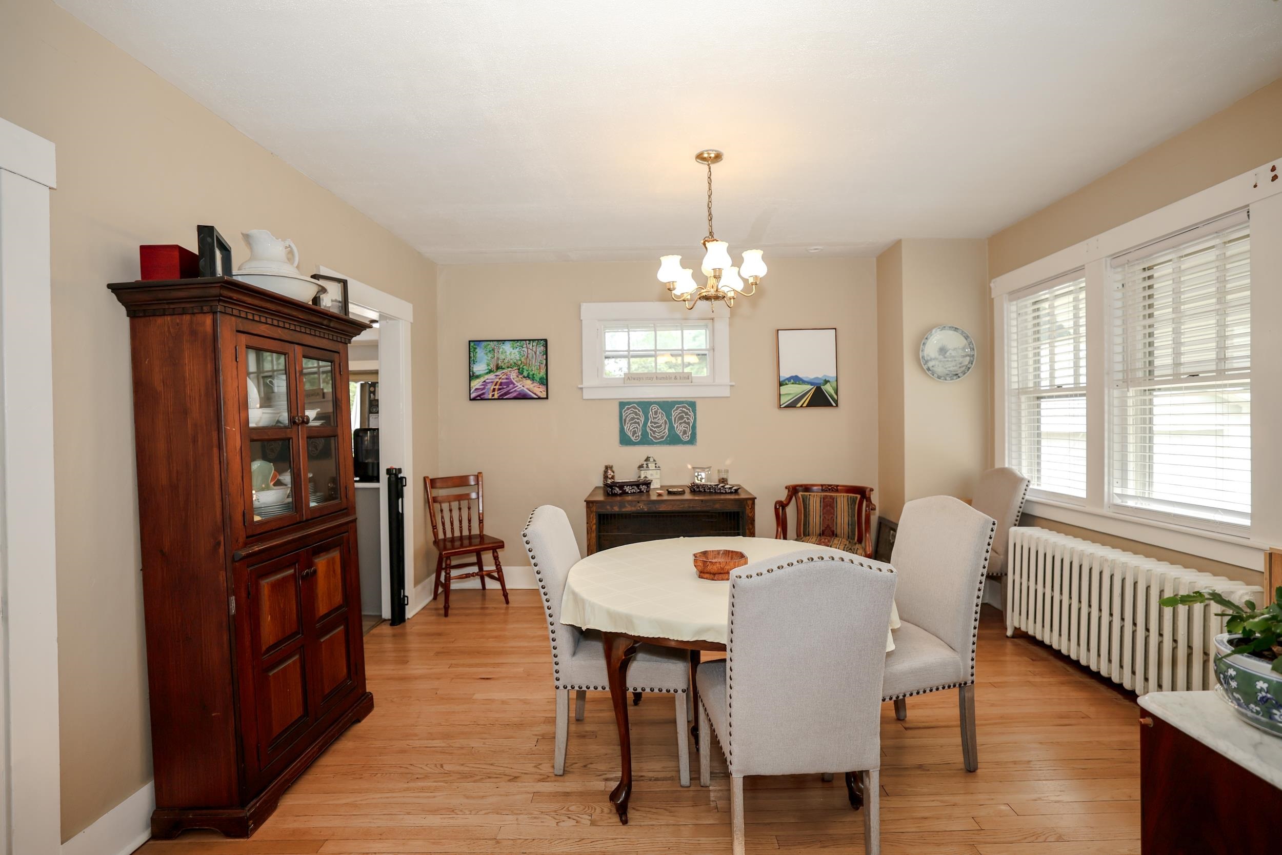 Dining room with a round table, upholstered chairs, dark china cabinet, and large windows.