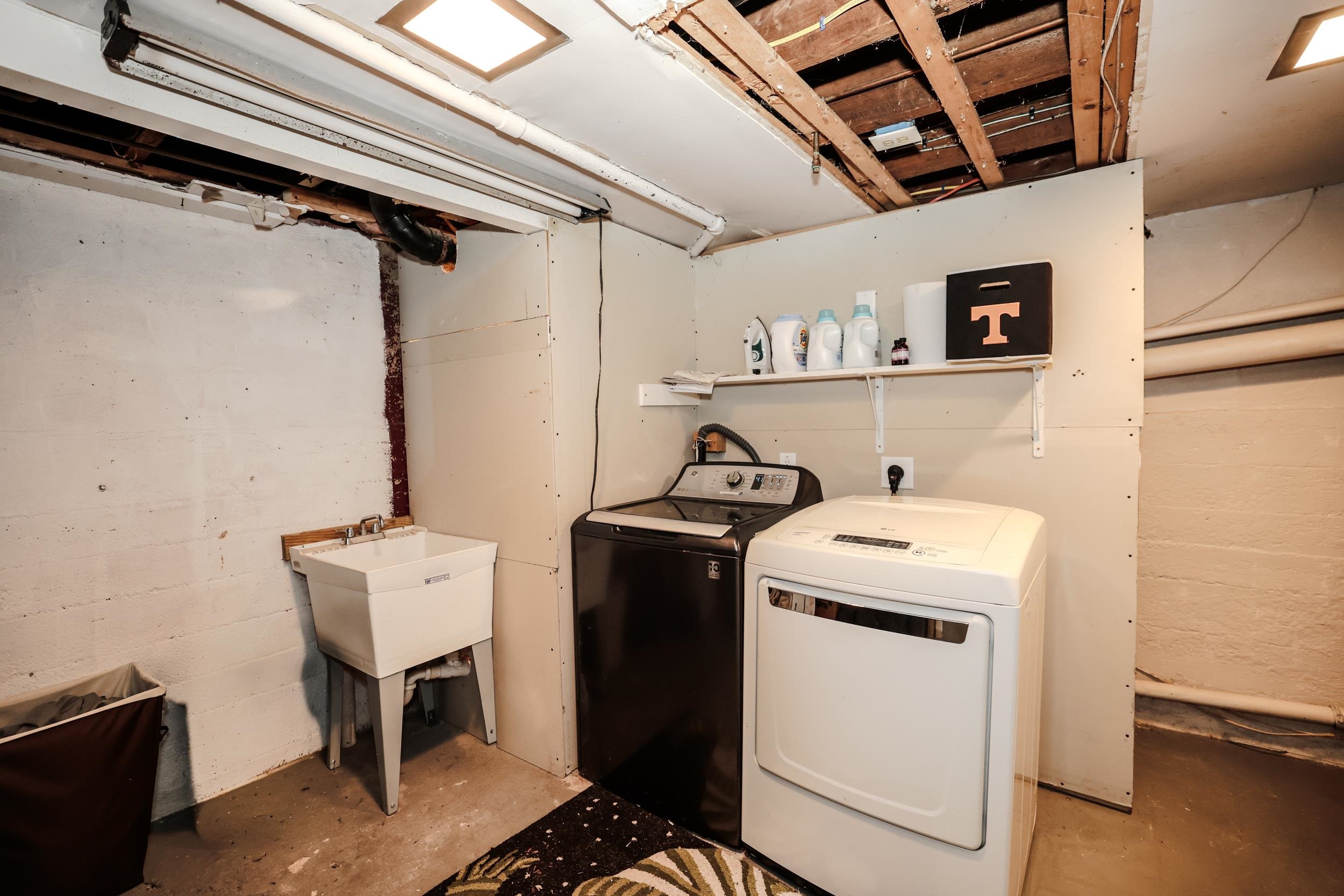 Basement laundry room with washer, dryer, utility sink, and exposed ceiling joists.