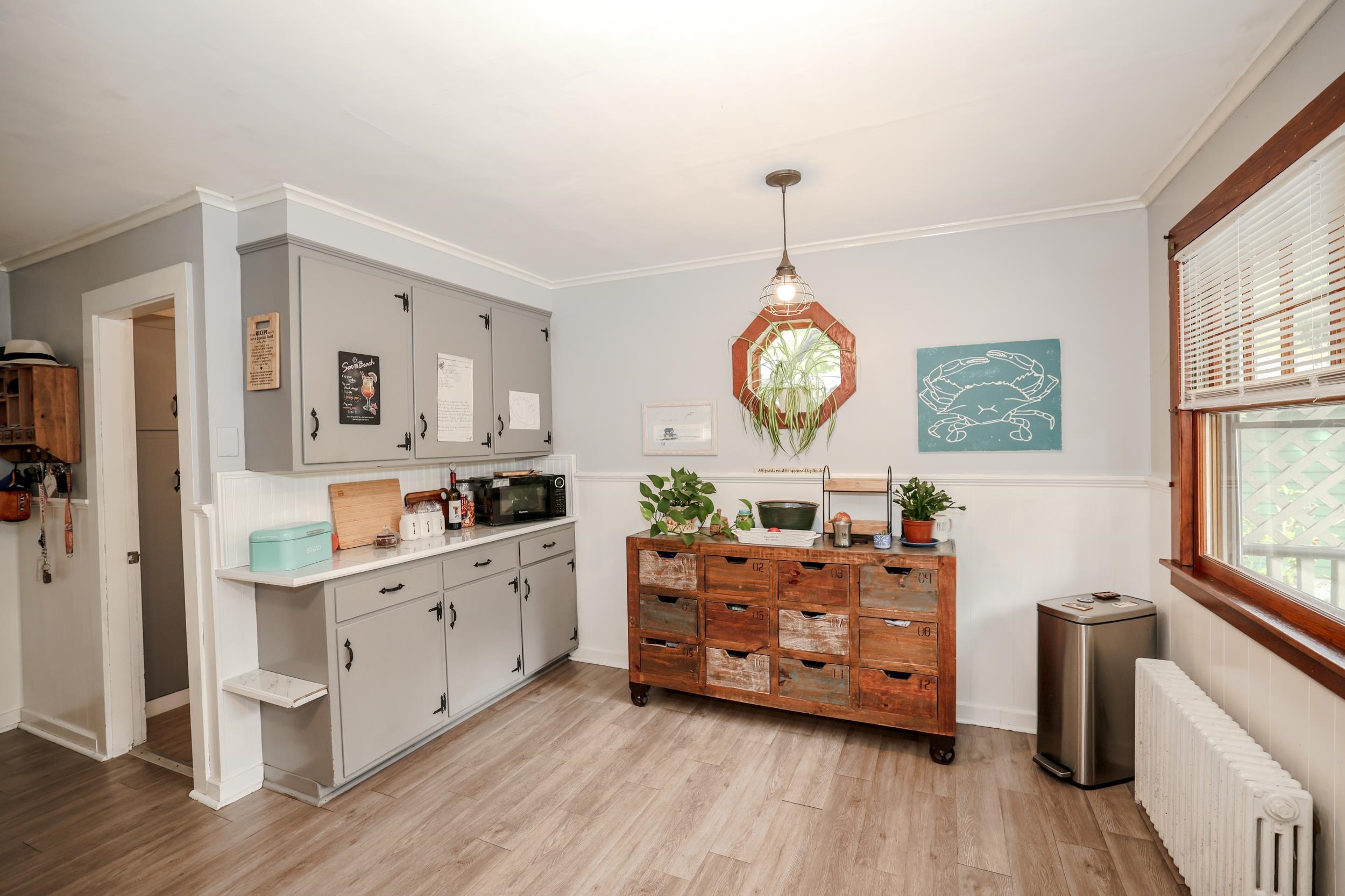 Kitchen with gray built-in cabinets, a rustic rolling drawer island, plants, and a large wood-trimmed window.
