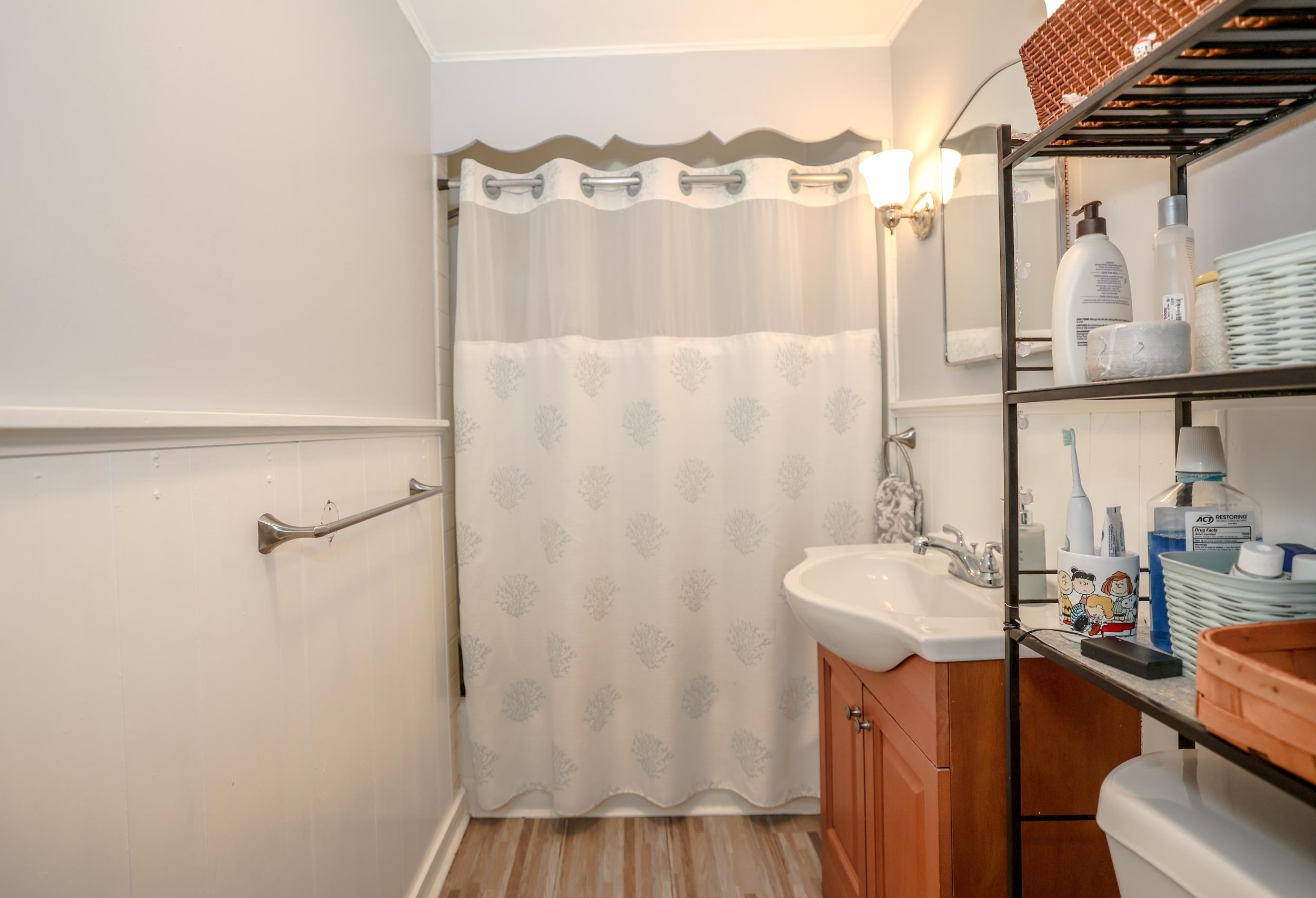 Bathroom with a patterned shower curtain, wood vanity, and open shelving with toiletries.