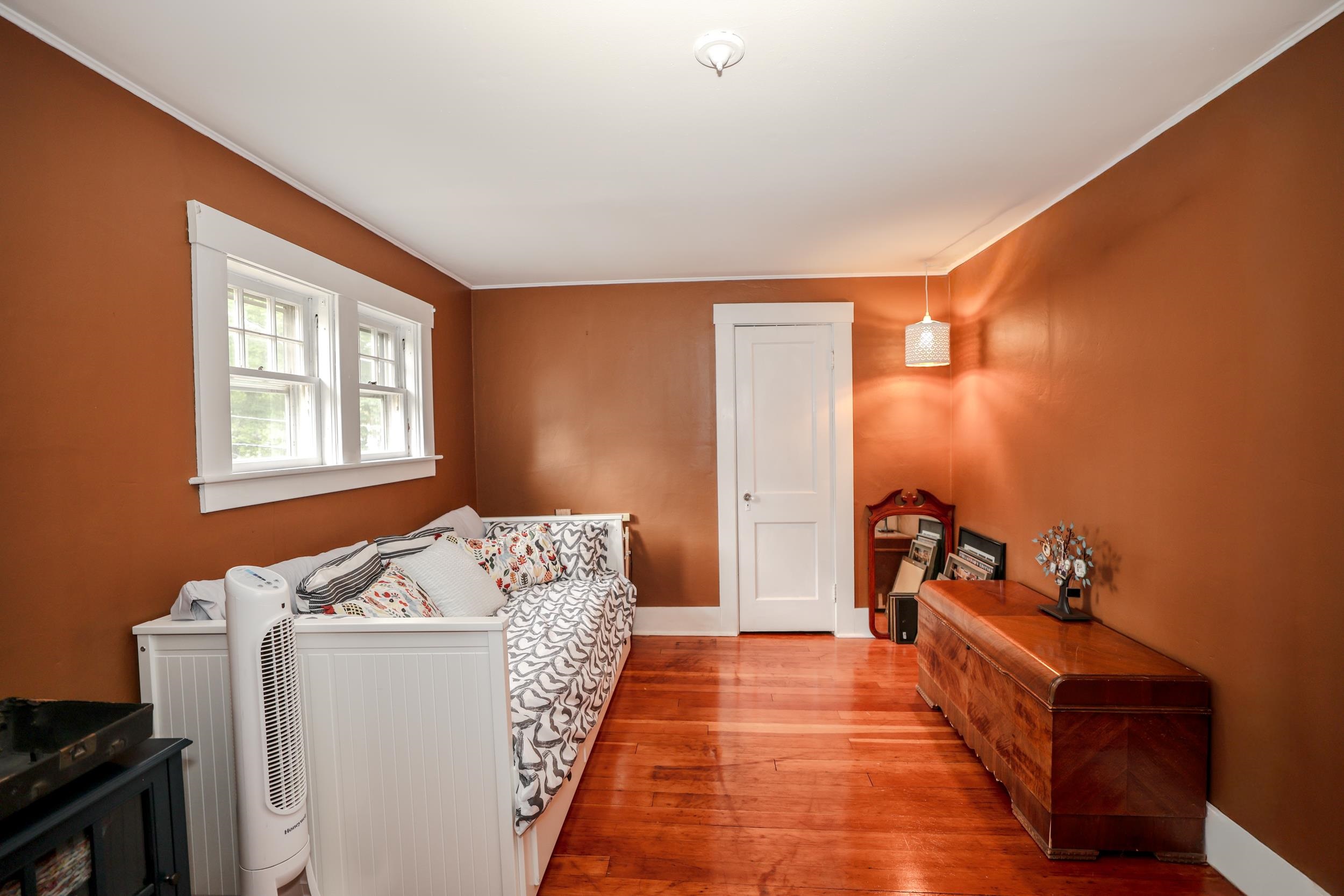 Bedroom with a white daybed beneath two windows and a wooden chest against burnt-orange walls.
