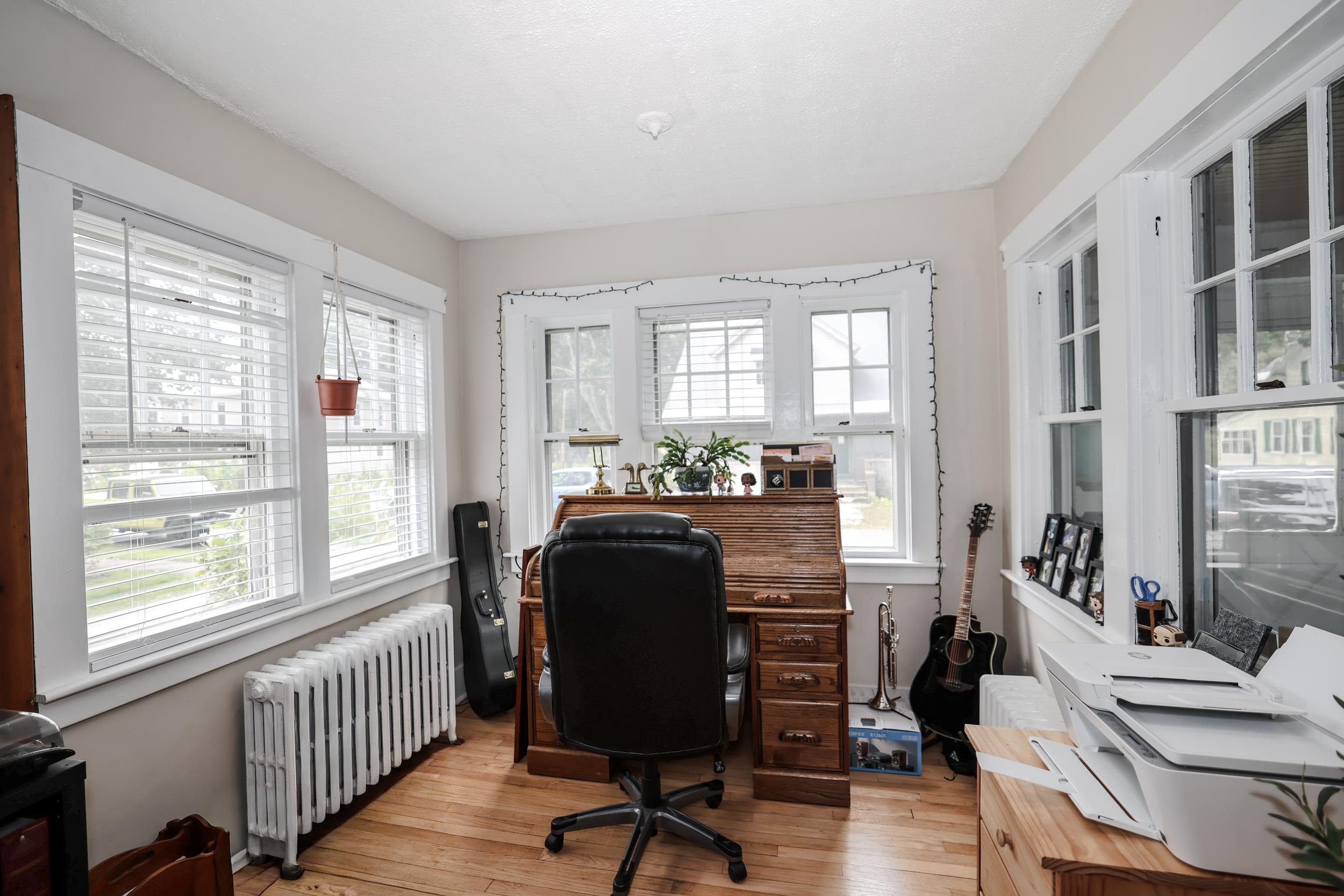 Bright home office with a wooden desk, large windows, hardwood floors, and a guitar.