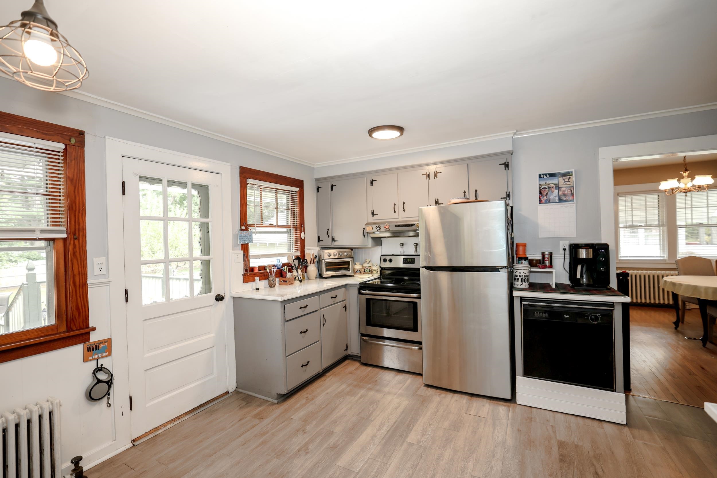 Kitchen with gray cabinets, stainless steel appliances, wood-trimmed windows, and a glass-paneled door.