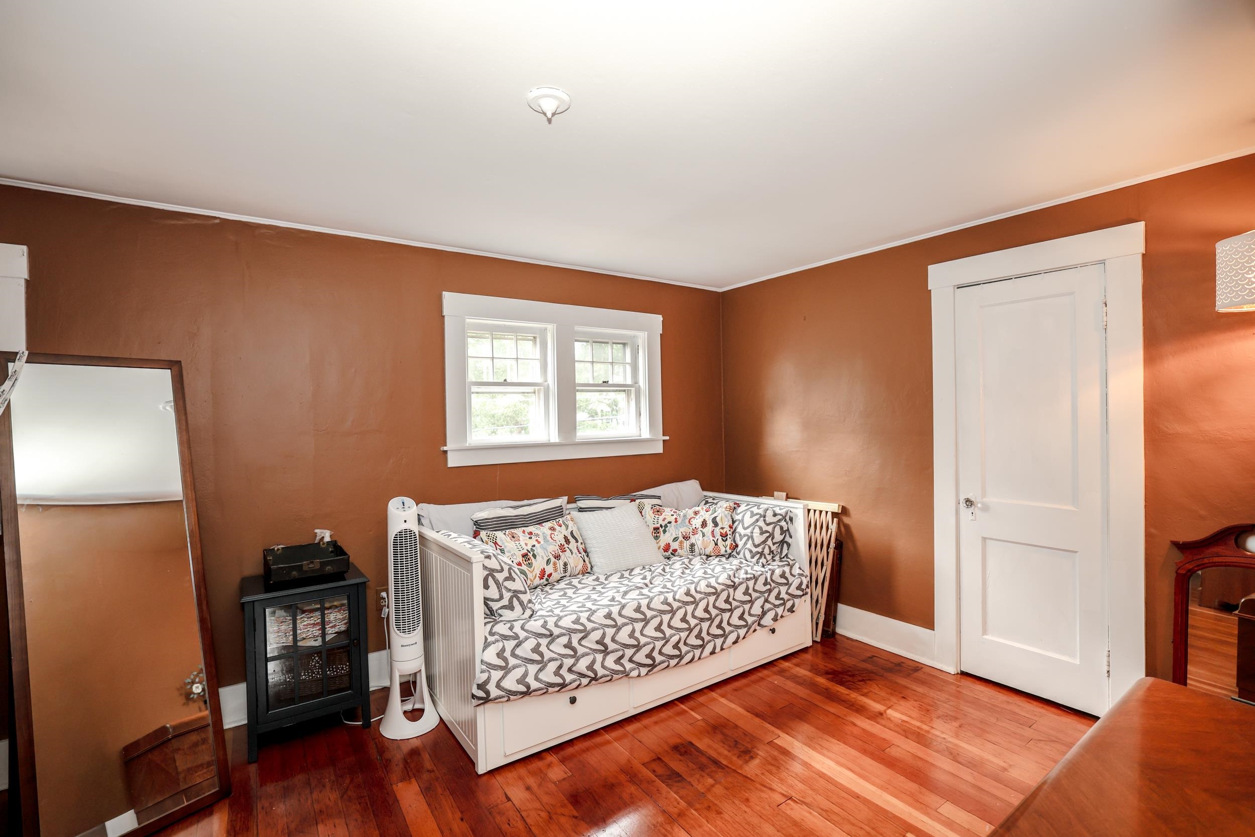 Bedroom with a white daybed beneath two windows and polished hardwood floors.