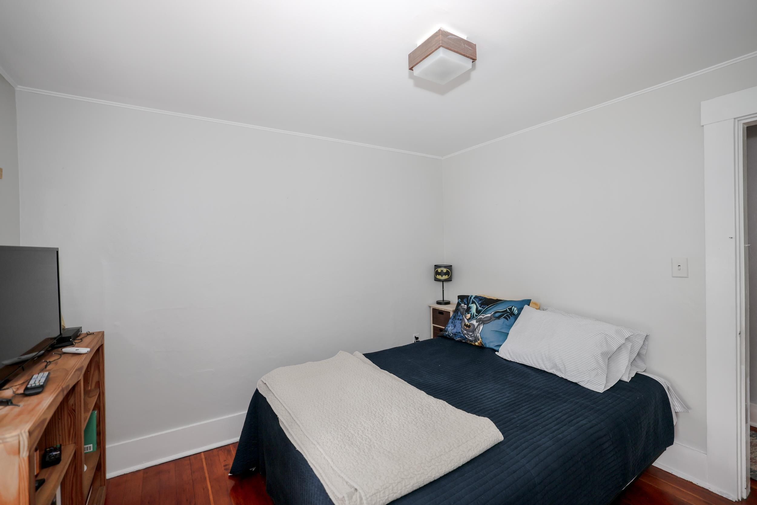 Bedroom with a navy bedspread, white quilt, and Batman-themed pillow and lamp.