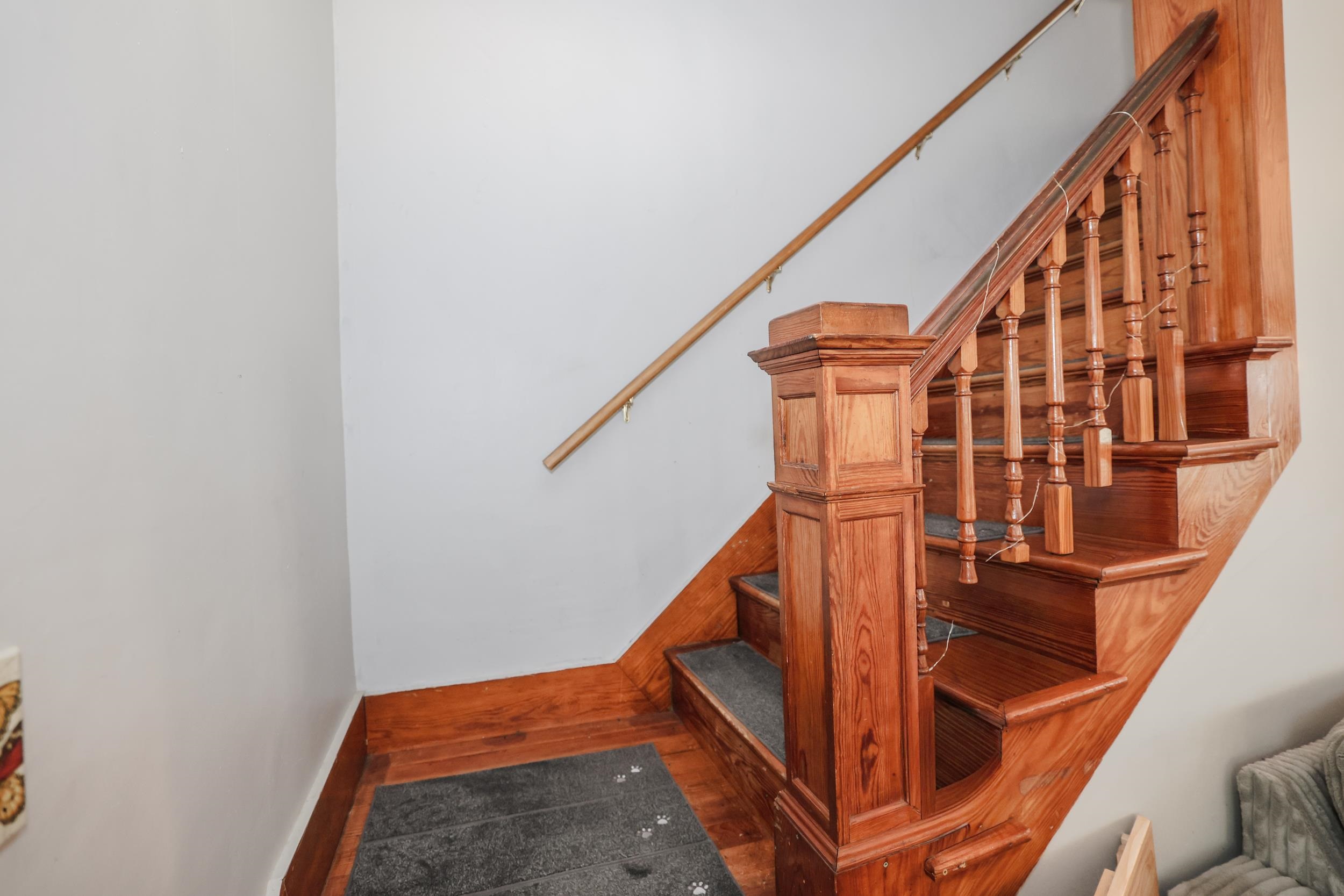 Wooden staircase with turned balusters and gray carpet runners on the steps.