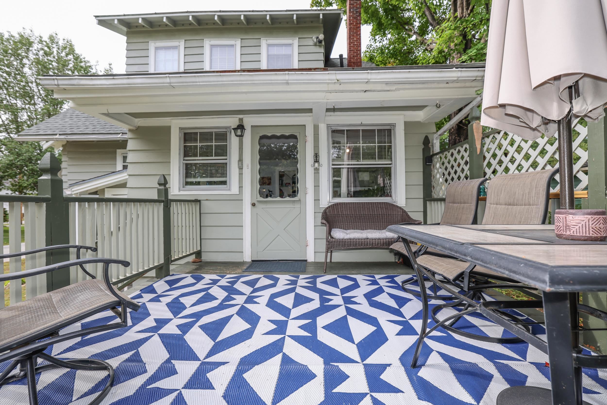 Covered front porch with a blue geometric rug, patio table, chairs, and white lattice railing.