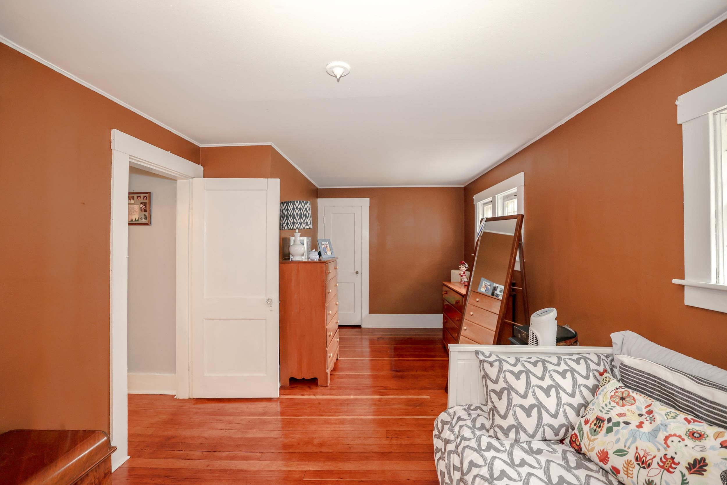 Furnished bedroom with rust-colored walls, hardwood floors, and a patterned daybed.