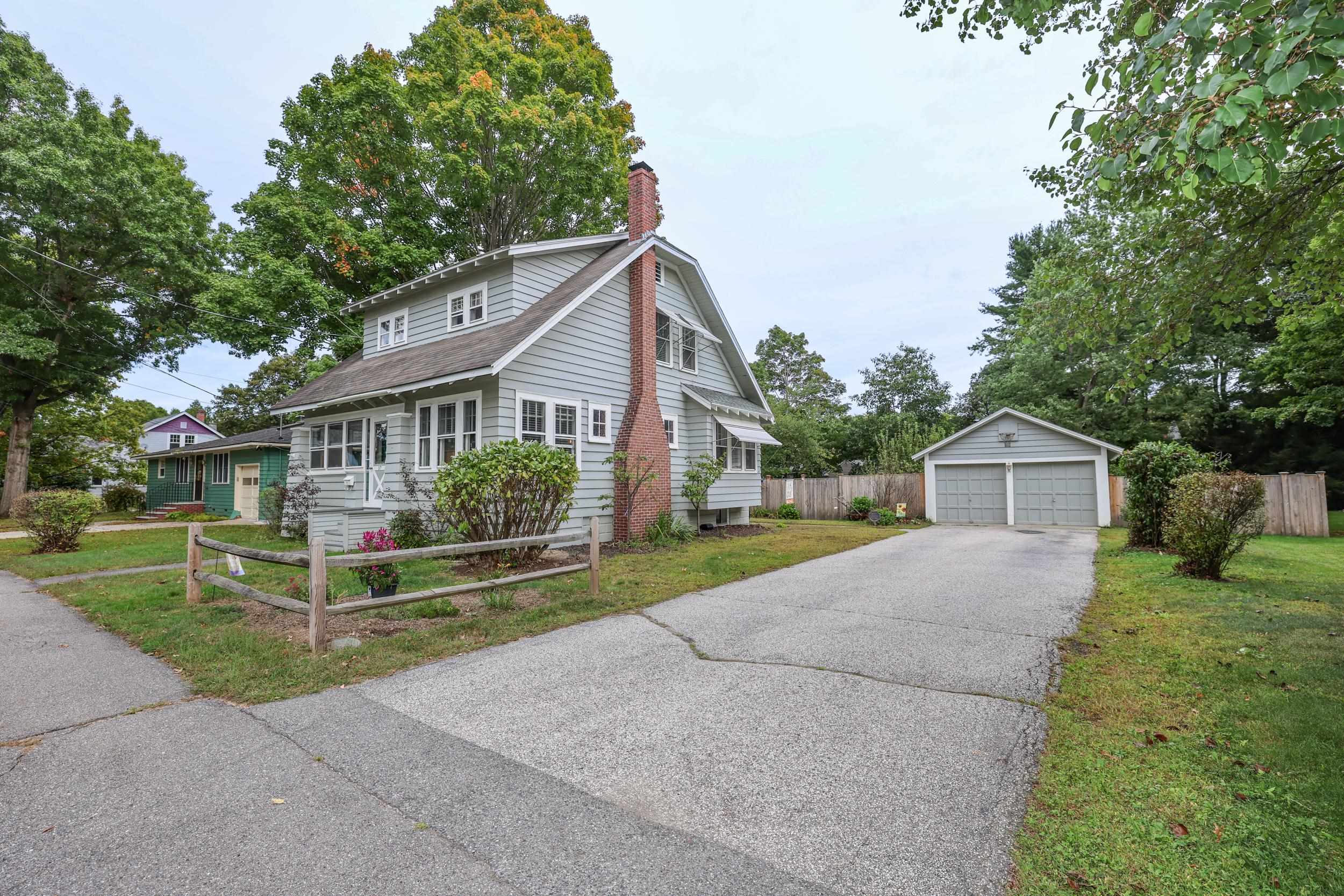 Gray two-story home with a brick chimney, detached garage, and wide paved driveway.