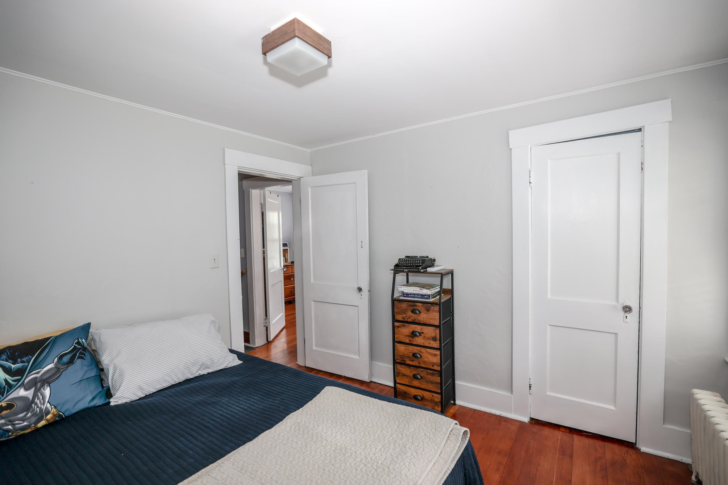 Bedroom with a dark blue bed, wood floors, and a chest topped by a typewriter.