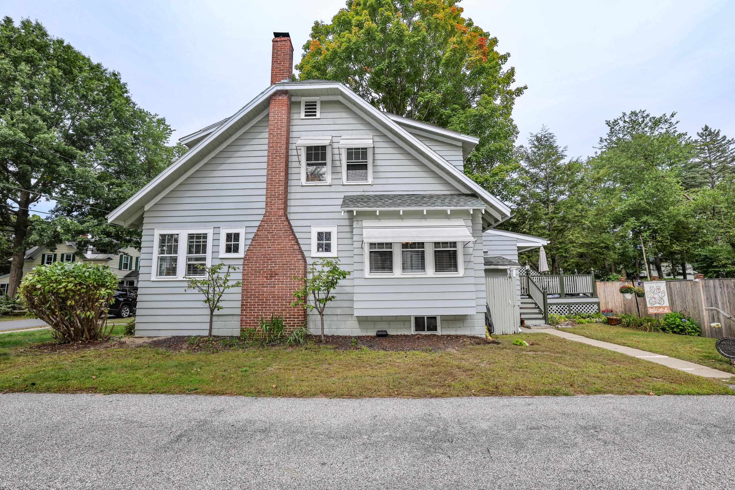 Gray gabled house with a tall brick chimney, white-trimmed windows, and fenced side deck.