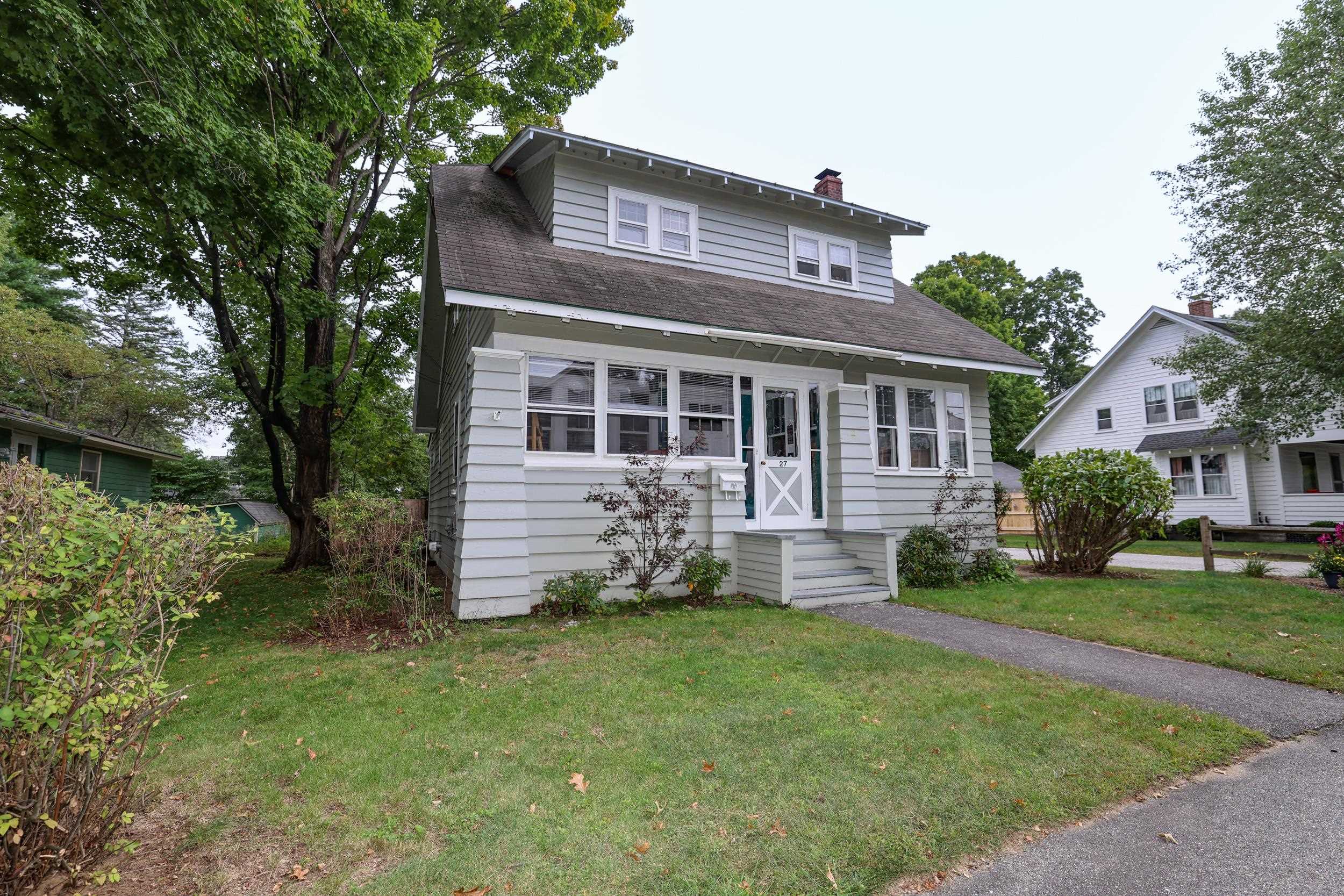 Light gray two-story house with a wide sloped roof, front steps, and mature trees.