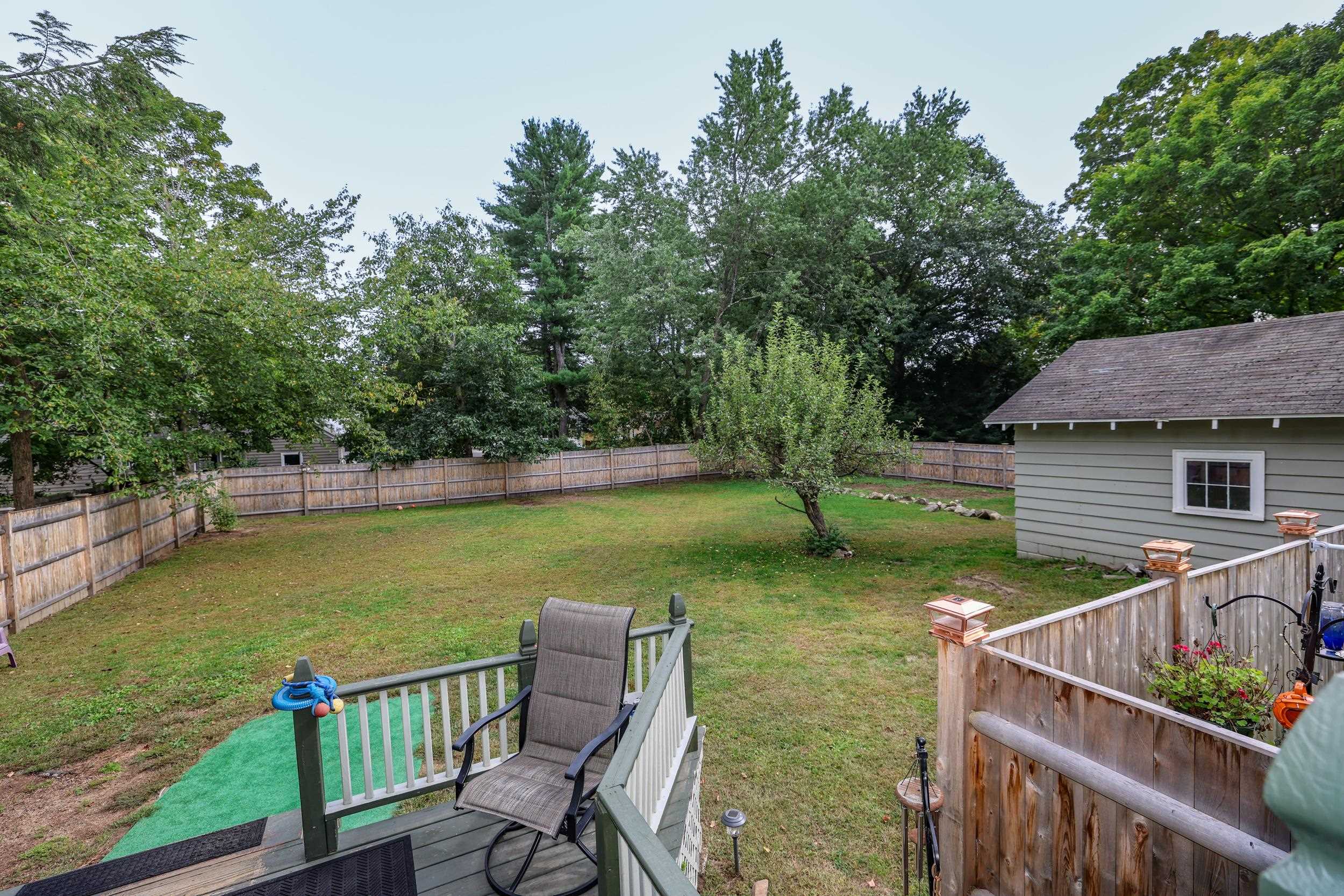 Fenced backyard with a broad lawn, mature trees, and a detached shed, viewed from a deck.