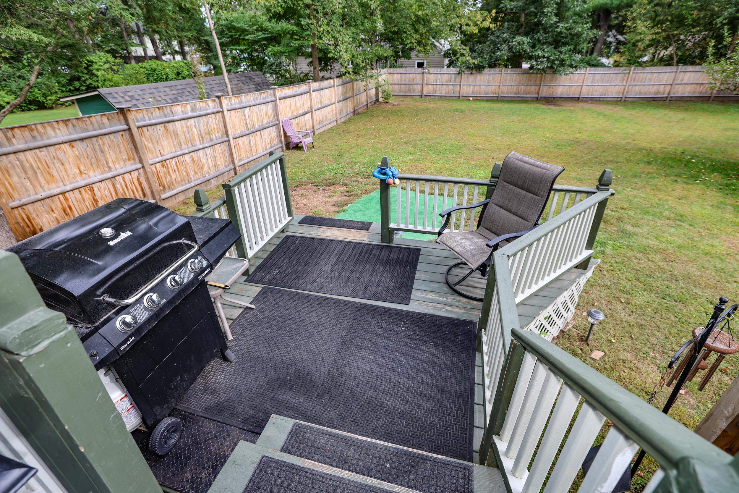 Raised deck with a black grill and chair overlooking a fenced grassy backyard.