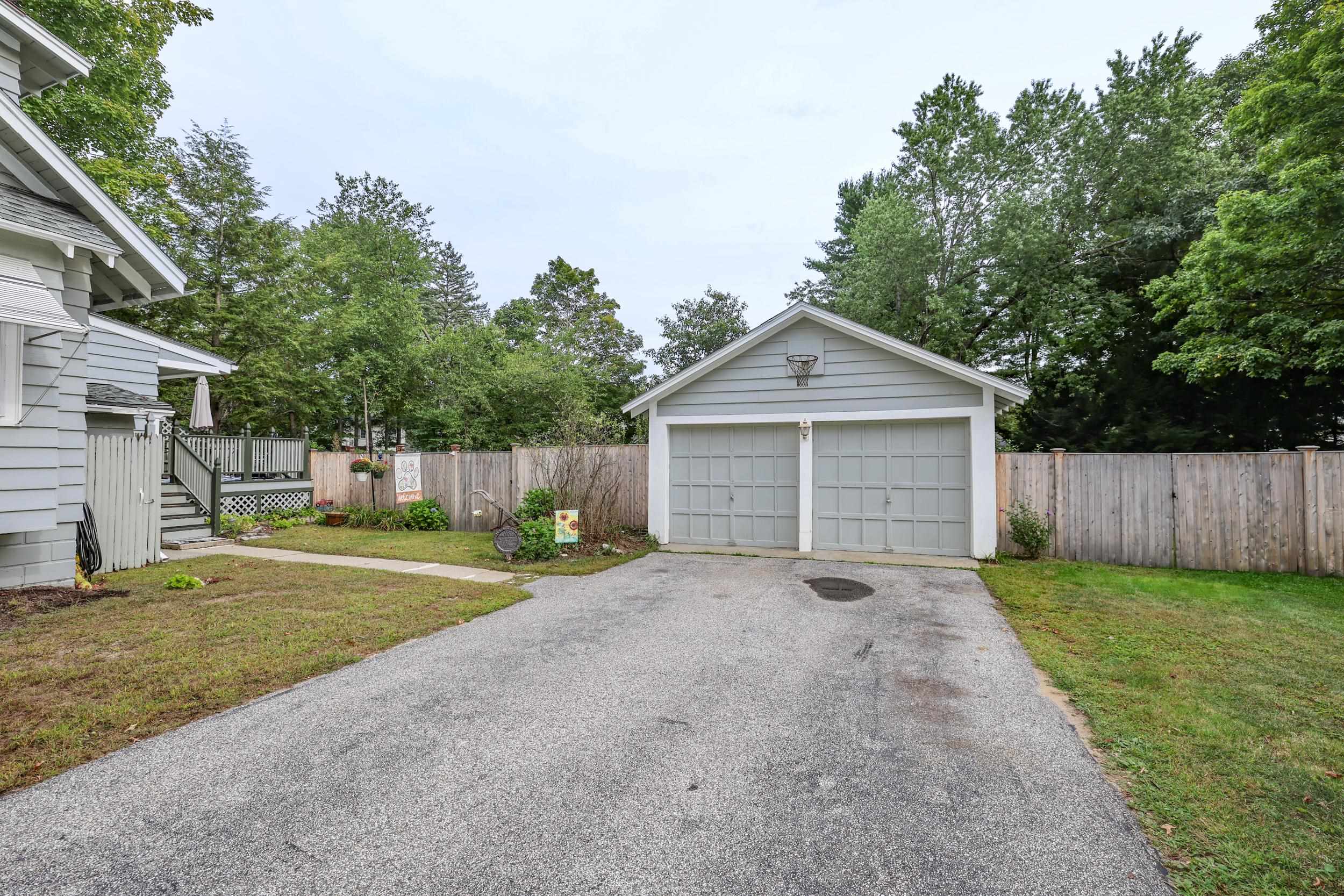 Detached two-car garage with a basketball hoop, wide driveway, and fenced yard.
