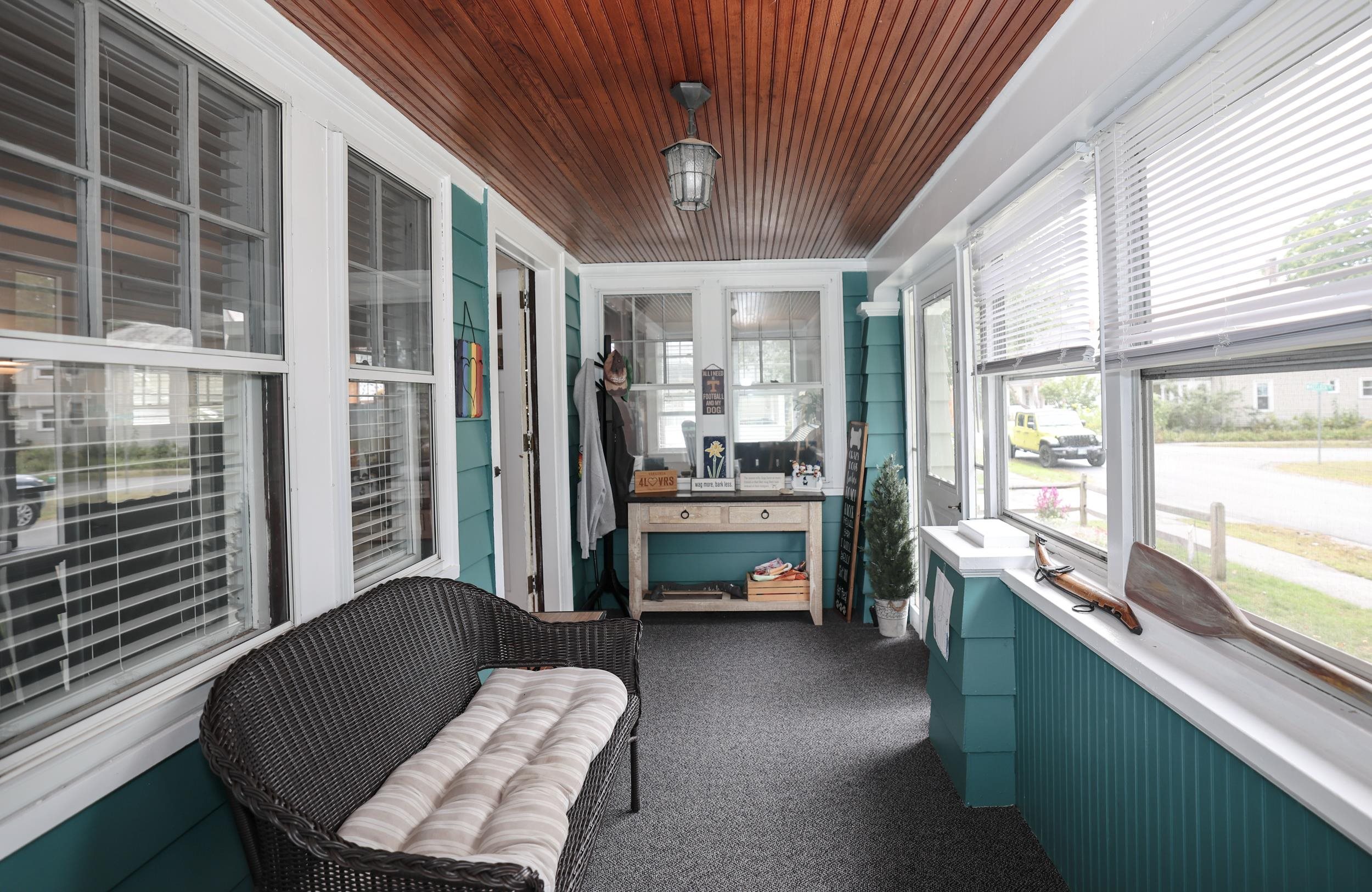 Enclosed sunroom with teal walls, a wood-paneled ceiling, and a wicker loveseat by the windows.