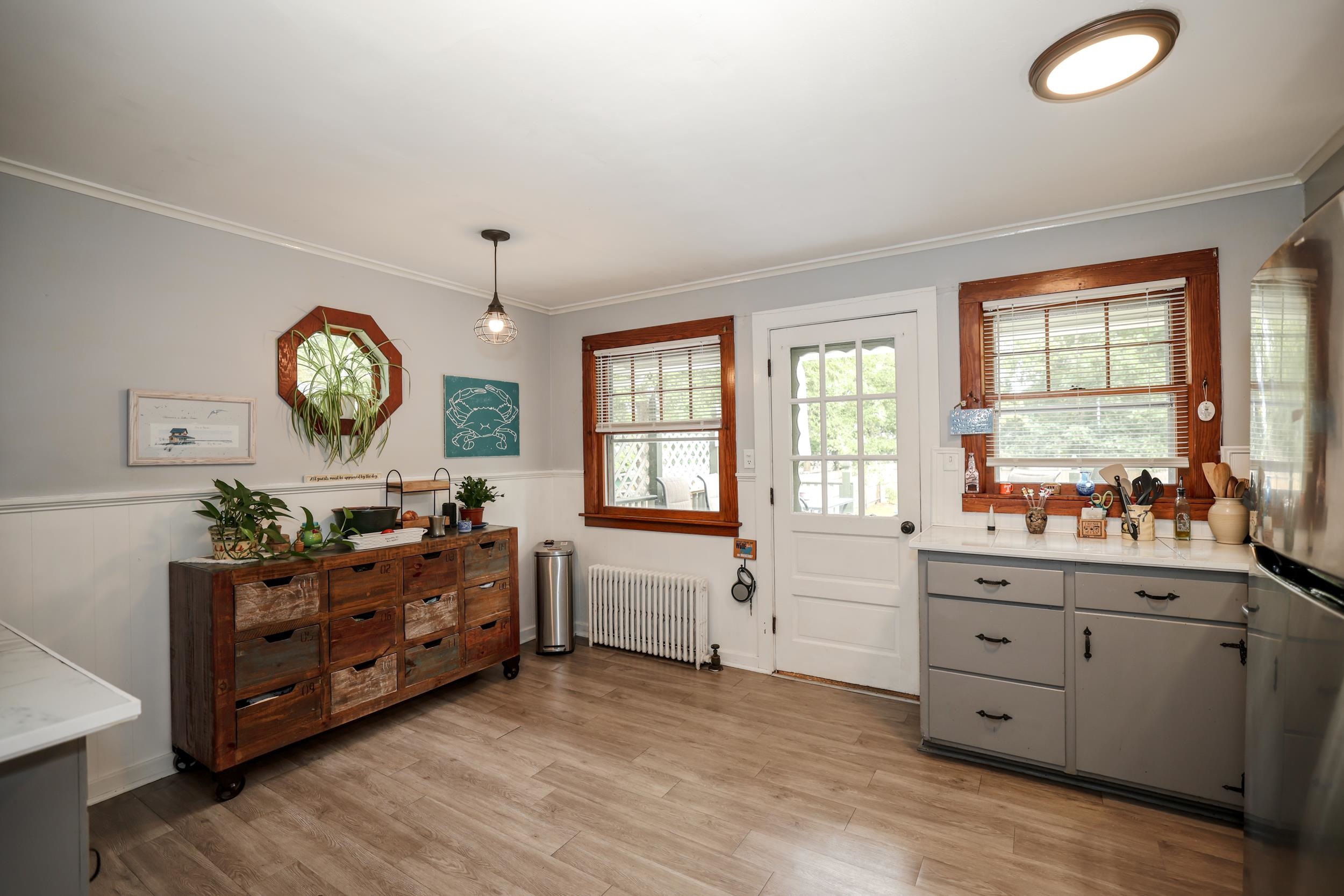 Kitchen with gray cabinets, wood-trimmed windows, and a rustic wooden drawer island topped with plants.