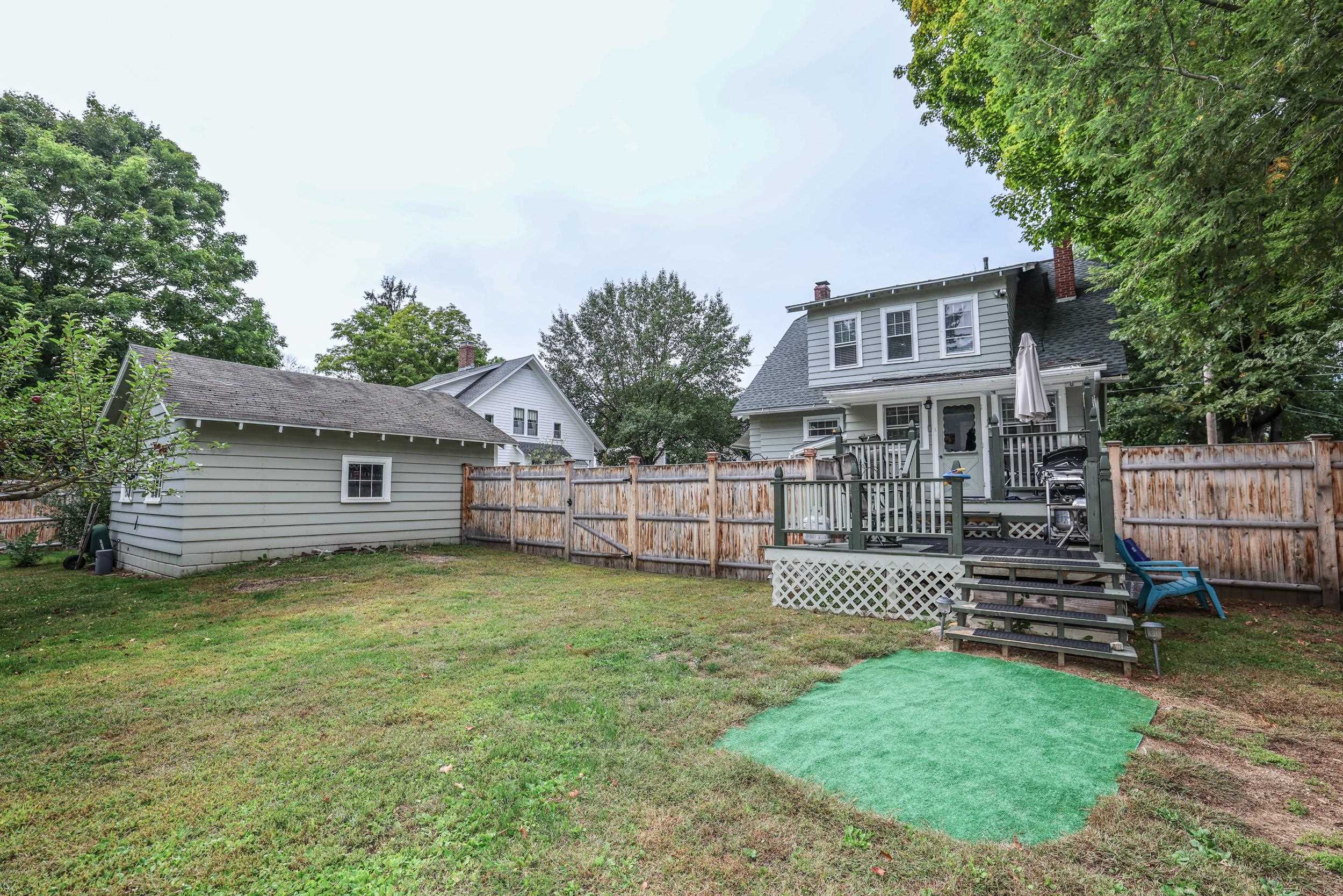 Gray two-story house with a raised deck and fenced backyard beside a detached garage.