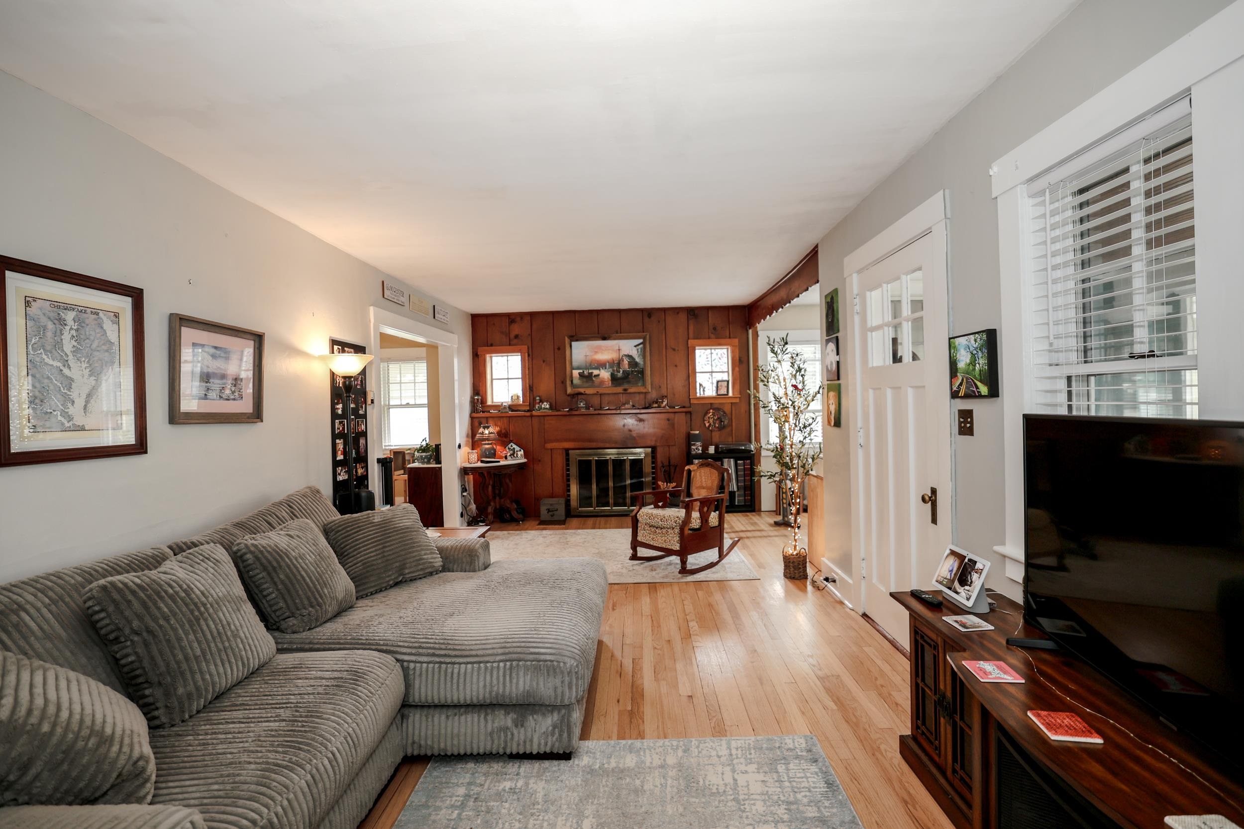 Living room with a gray sectional sofa, hardwood floors, and a wood-paneled fireplace wall.
