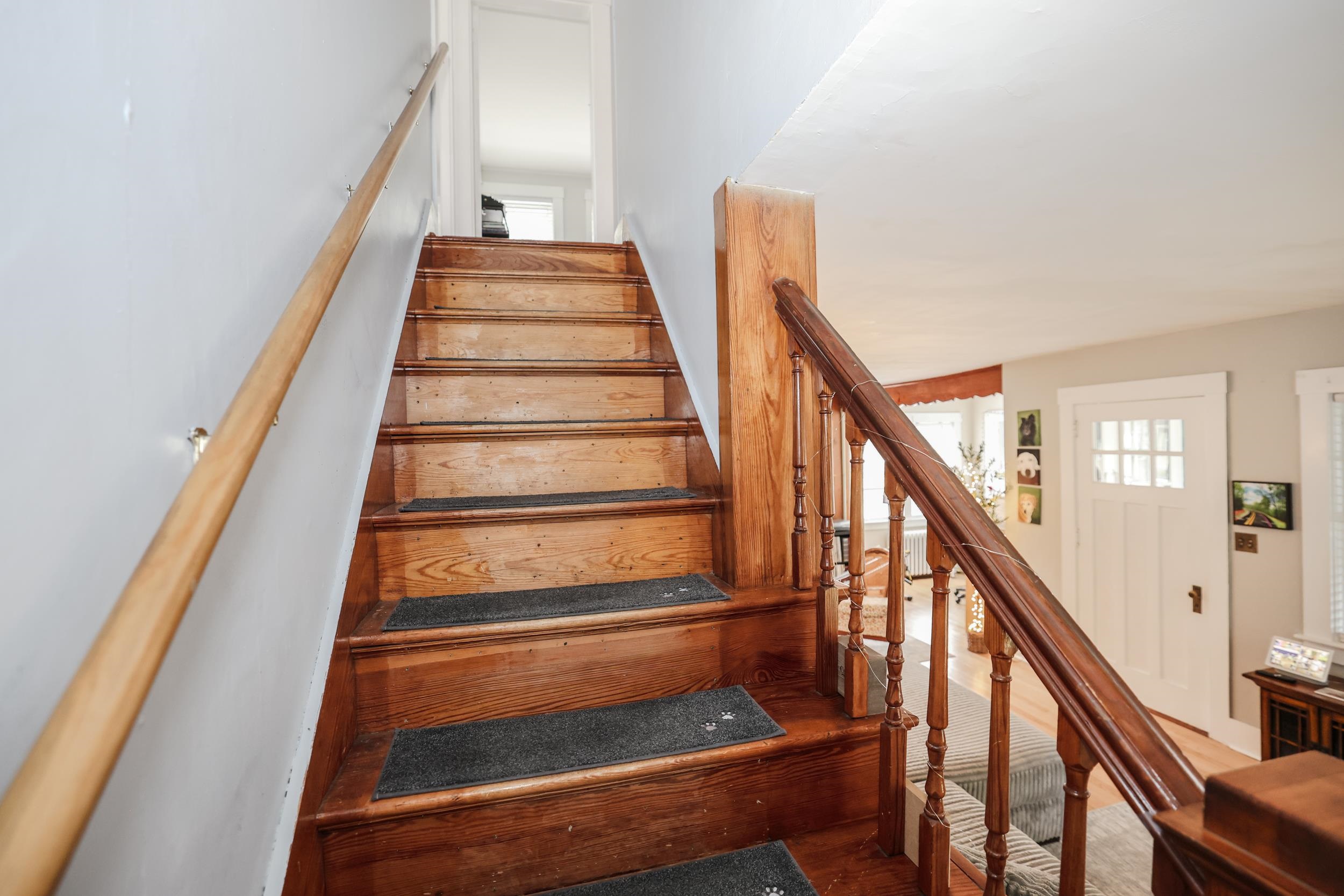 Wooden staircase with dark railings and gray tread mats overlooking a bright living area.