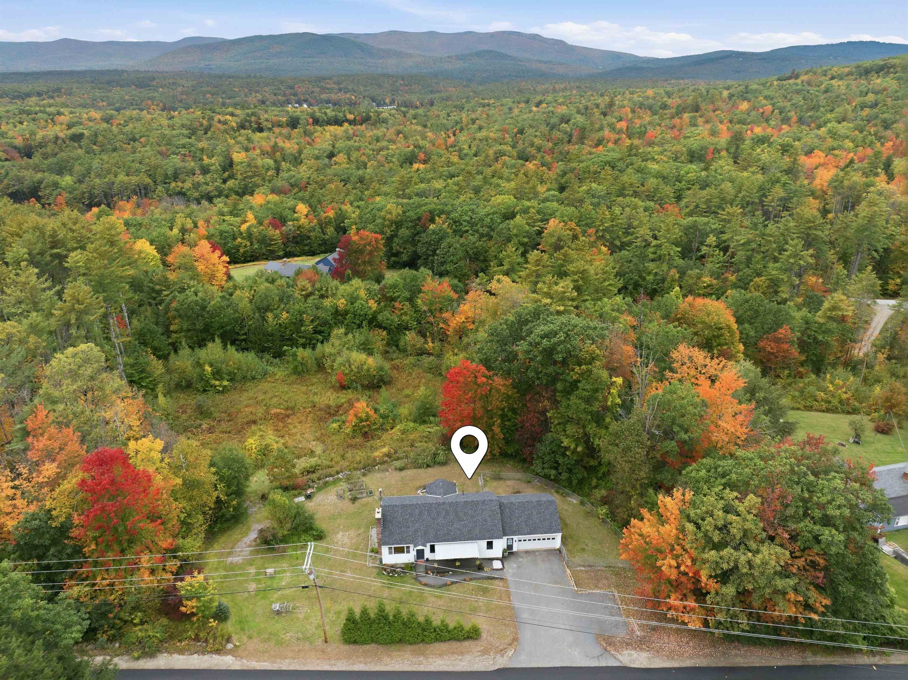 White home amid autumn woodland, with mountains in the distance.