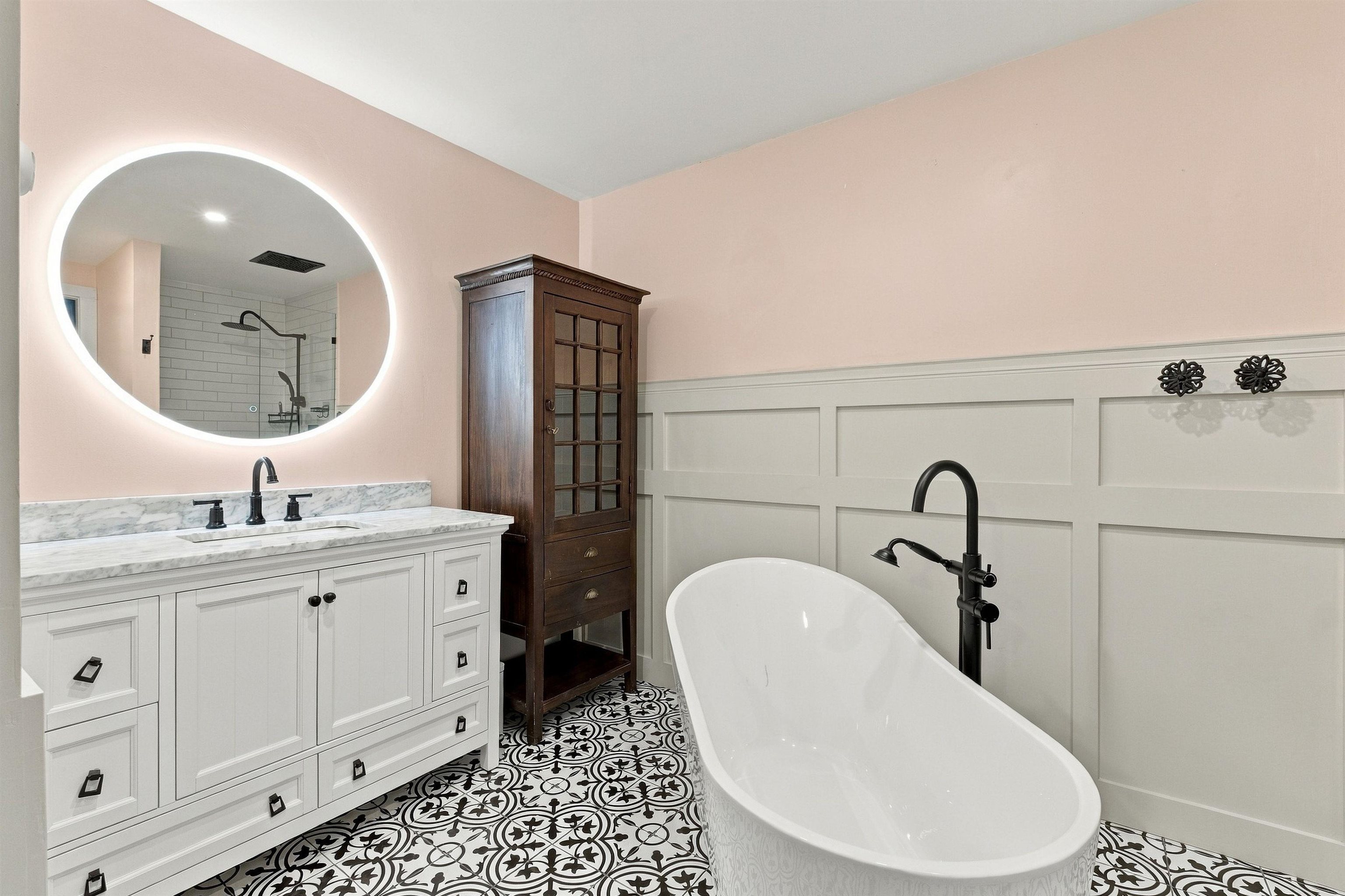 Bathroom with a freestanding soaking tub, backlit oval mirror, and patterned black-and-white tile floor.