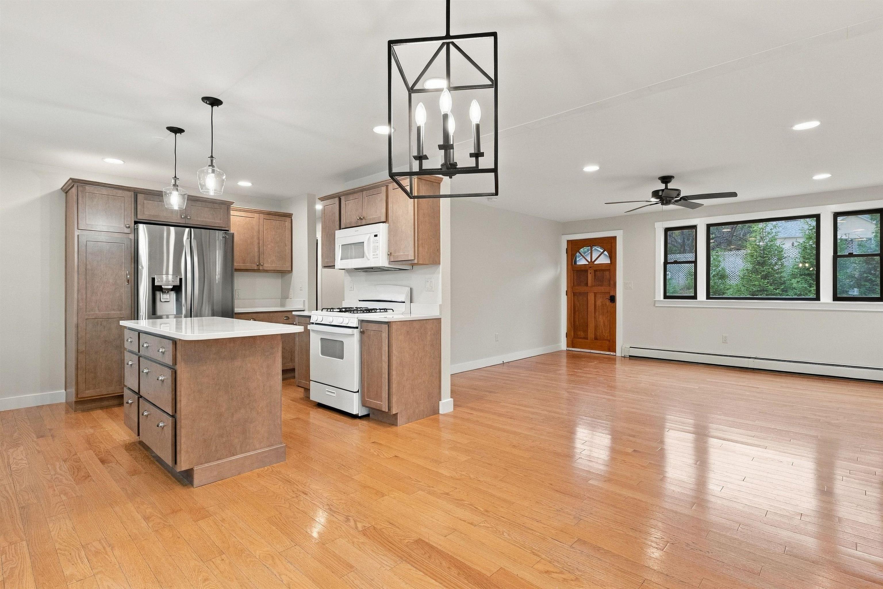 Open kitchen and dining area with a white-topped island, wood floors, and windows overlooking greenery.