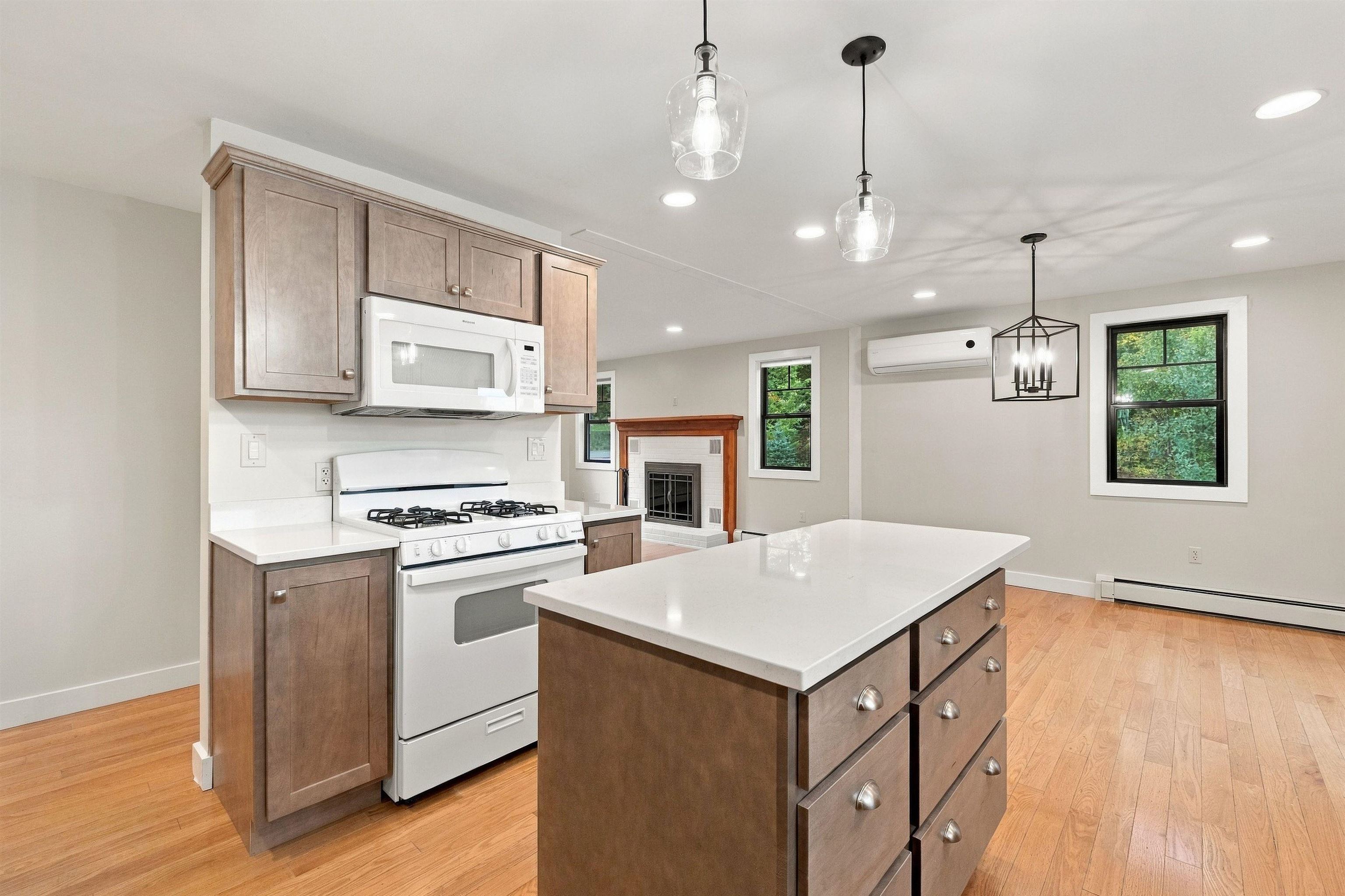 Kitchen with a large white-countertop island, brown cabinetry, gas range, and adjoining fireplace.