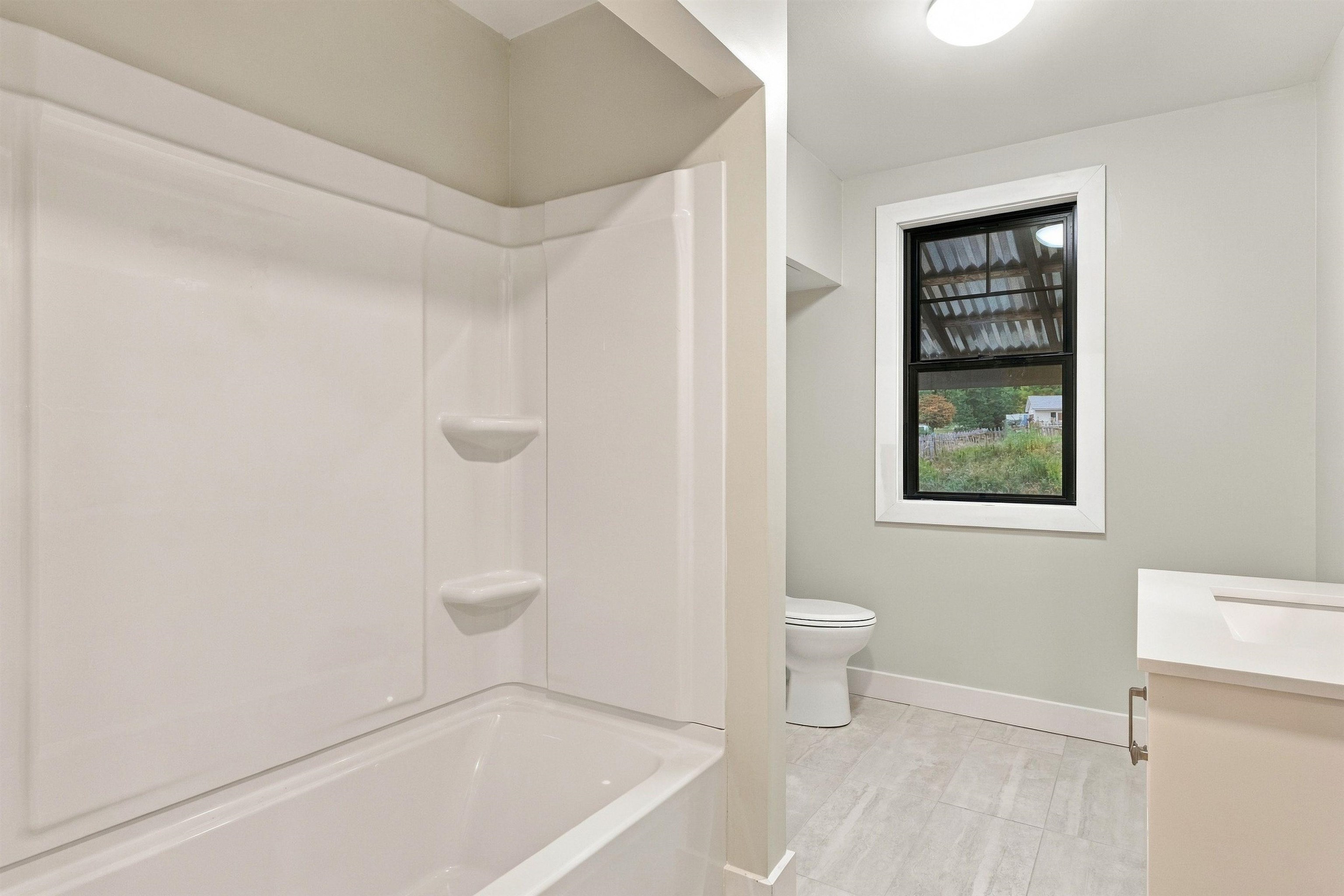 Bathroom with a white tub and shower, toilet, vanity, and black-framed window.
