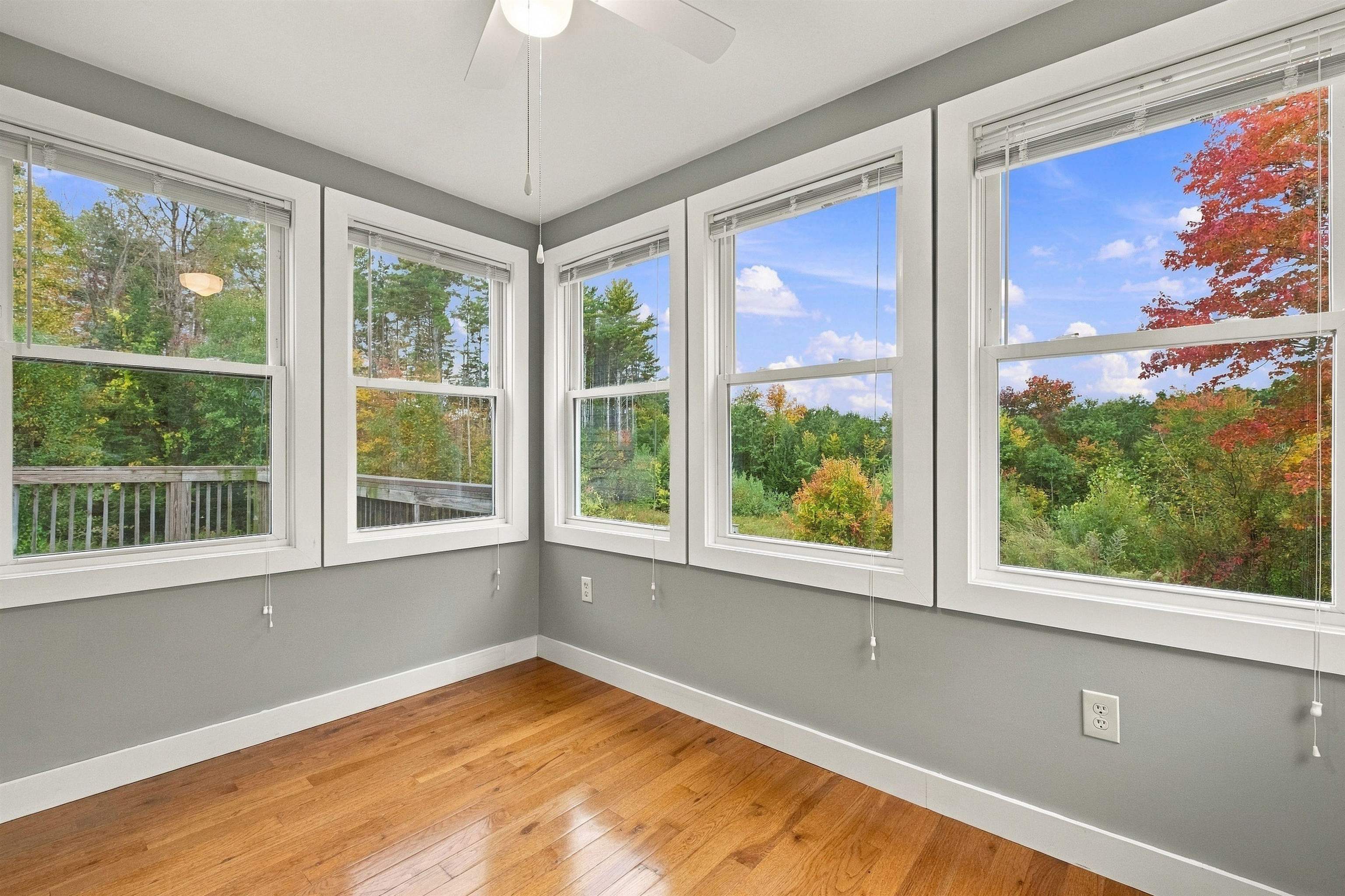 Empty room with hardwood floors and large windows overlooking autumn trees.
