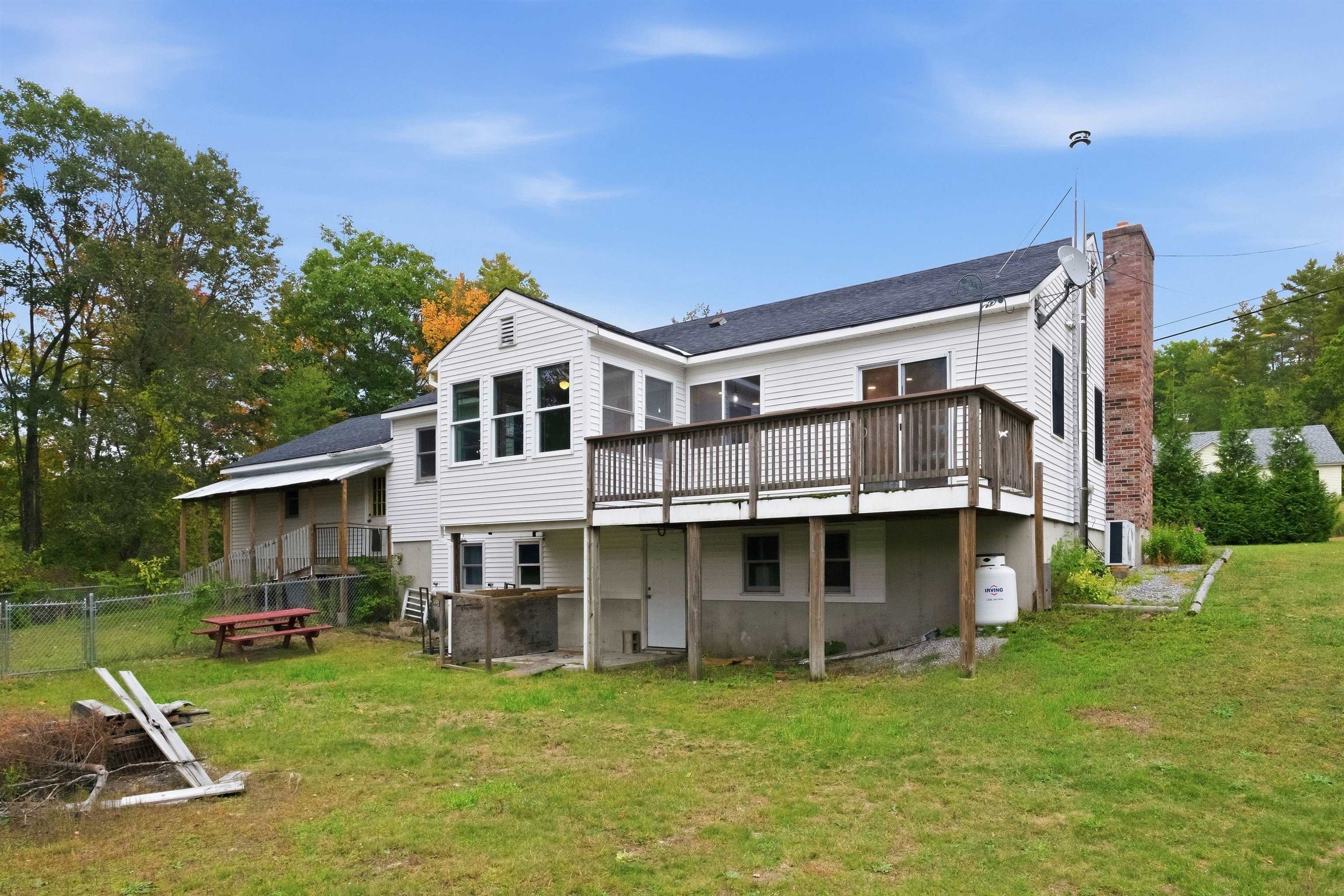 White-sided house with a raised wooden deck and brick chimney overlooking a grassy yard.