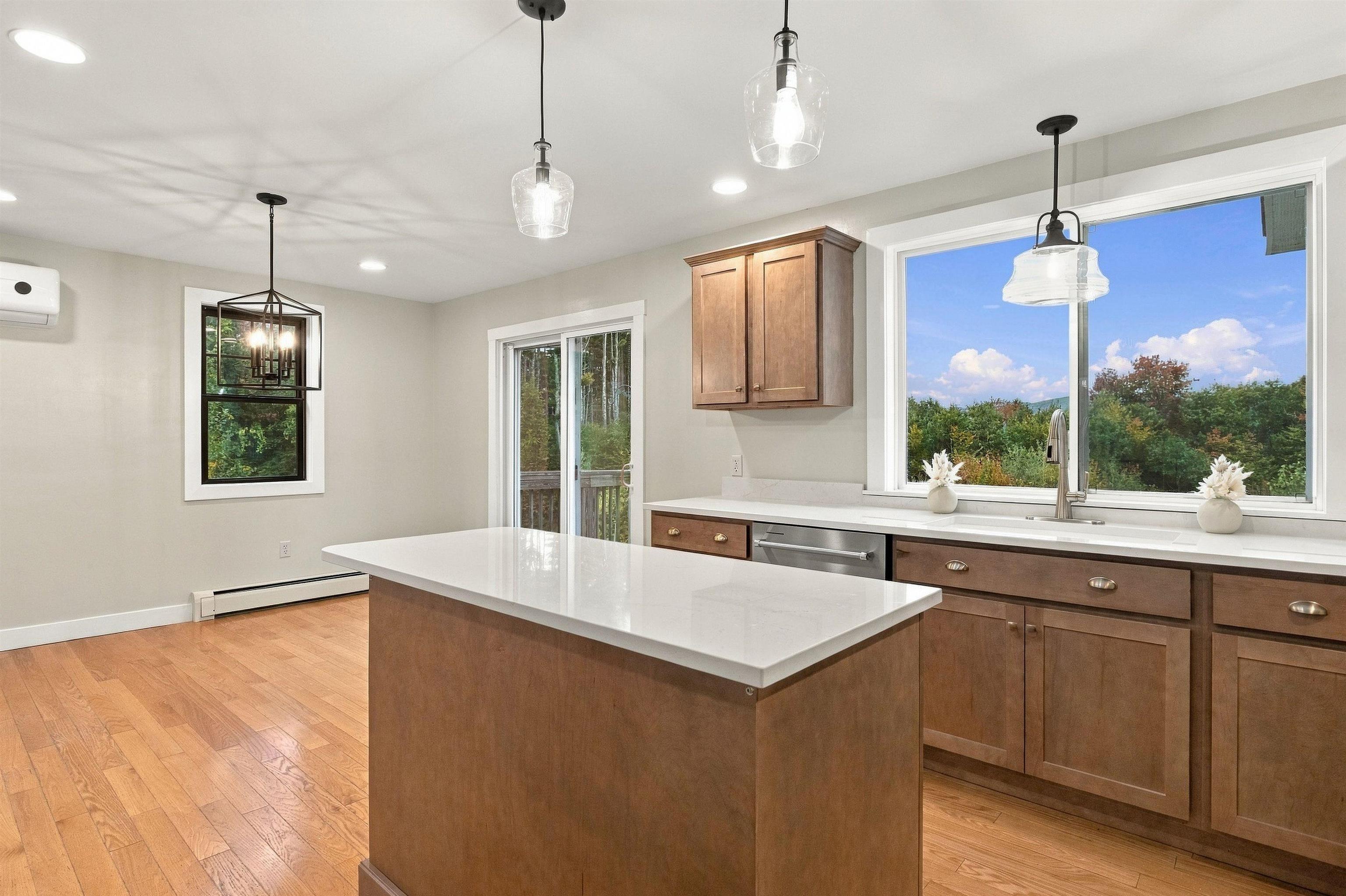 Kitchen with a large white island, warm wood cabinets, and a wide window overlooking trees.