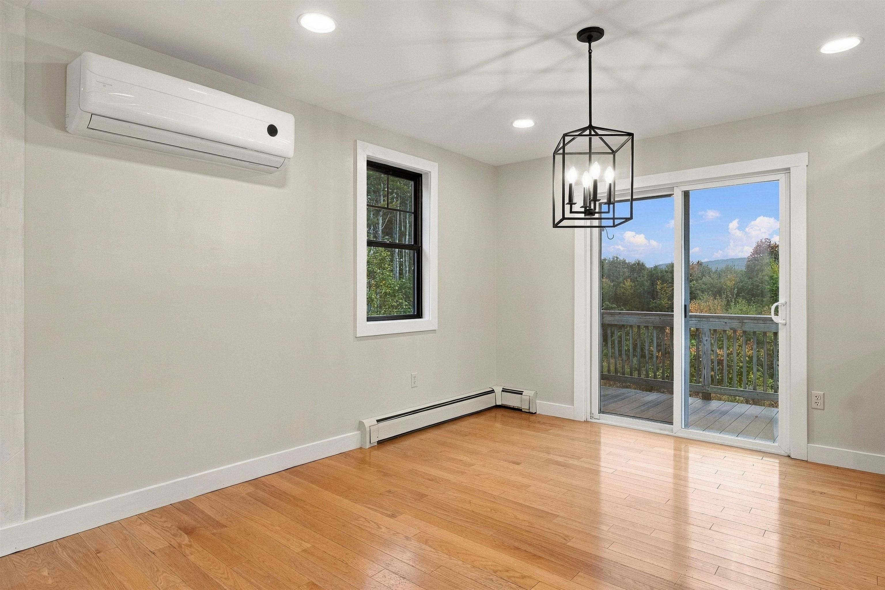 Unfurnished dining room with hardwood floors and a sliding glass door to a wooded deck.