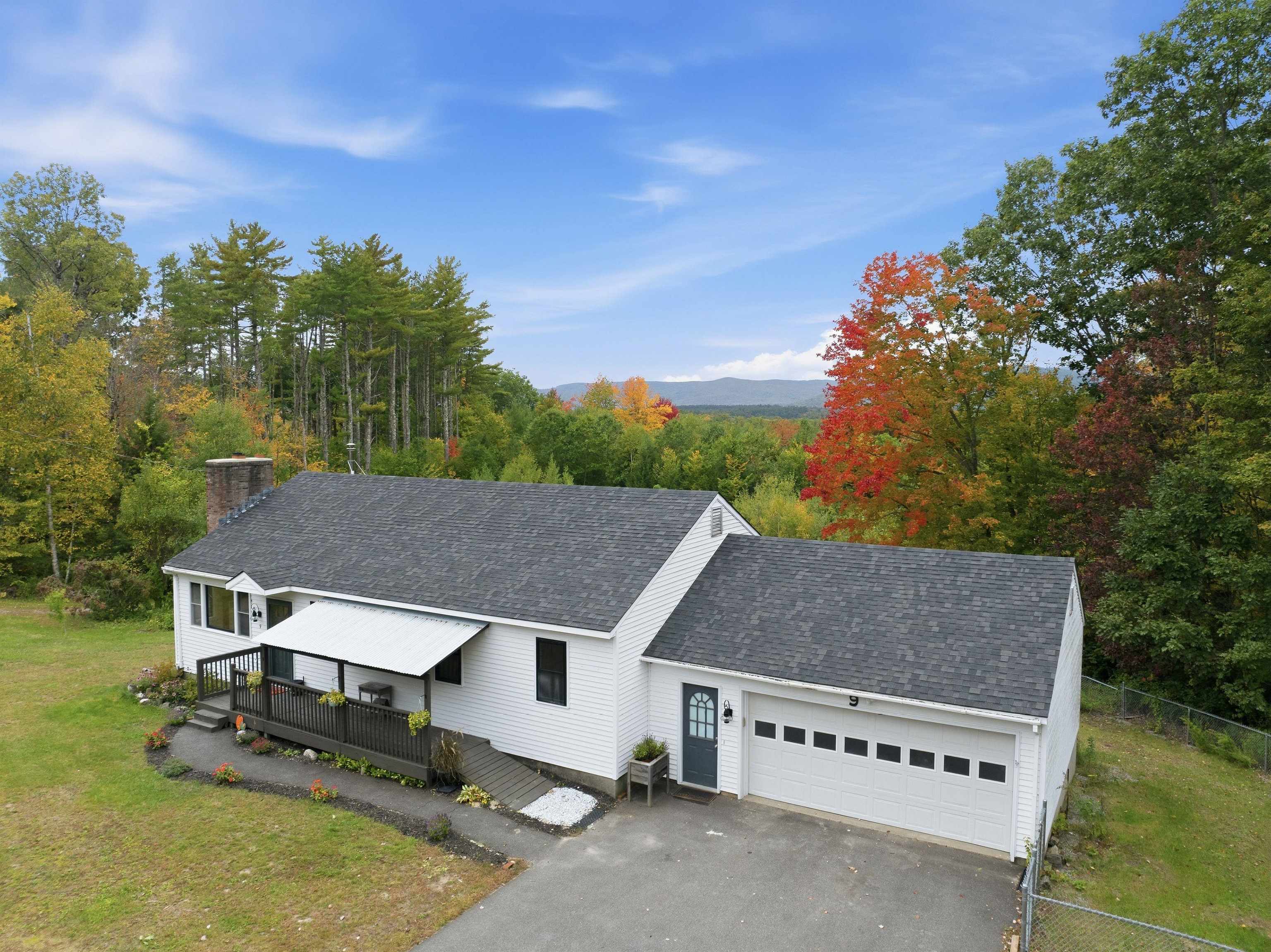 White home with attached garage and deck, backed by autumn woods and distant mountains.