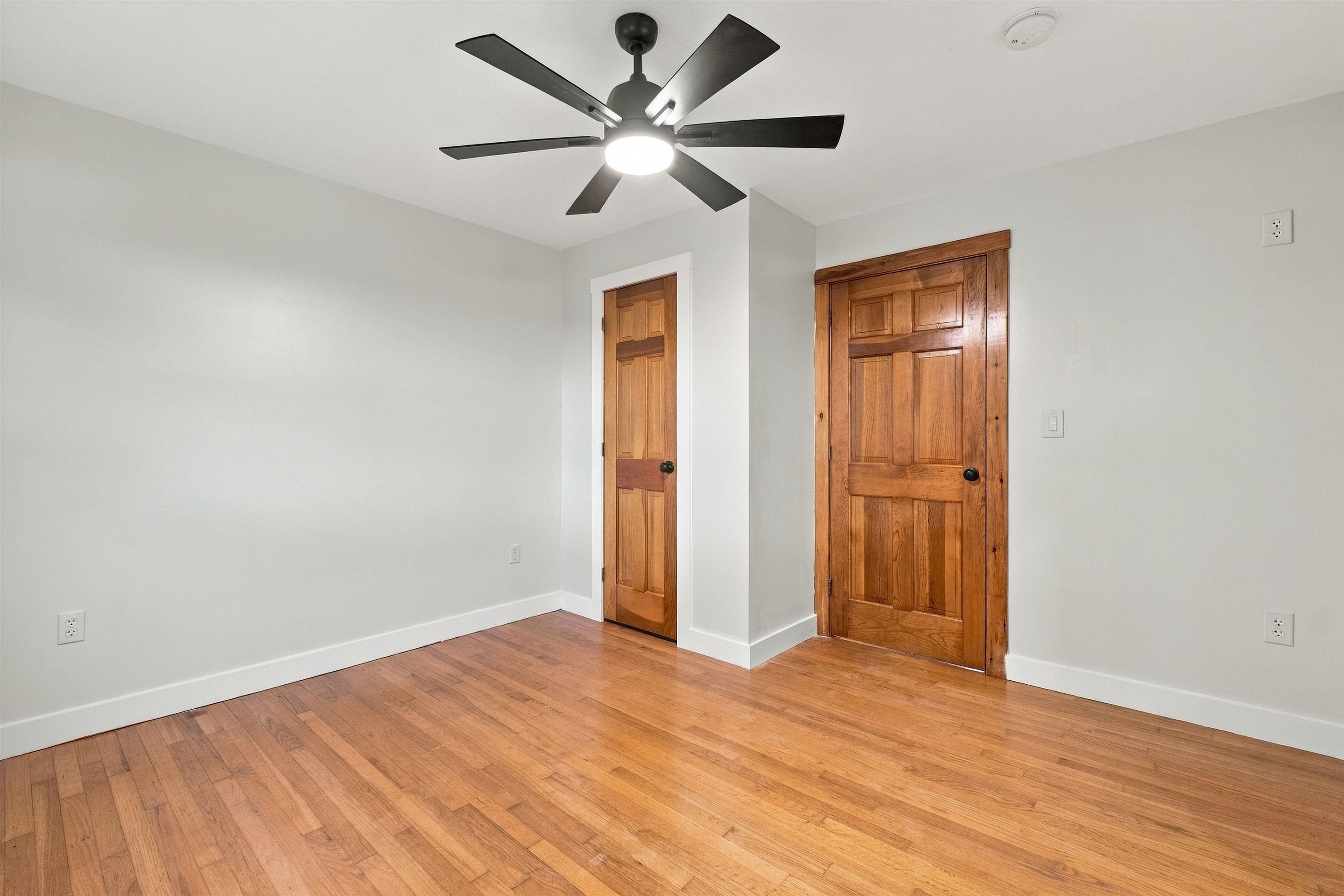 Empty room with hardwood floors, two wooden doors, and a ceiling fan with light.